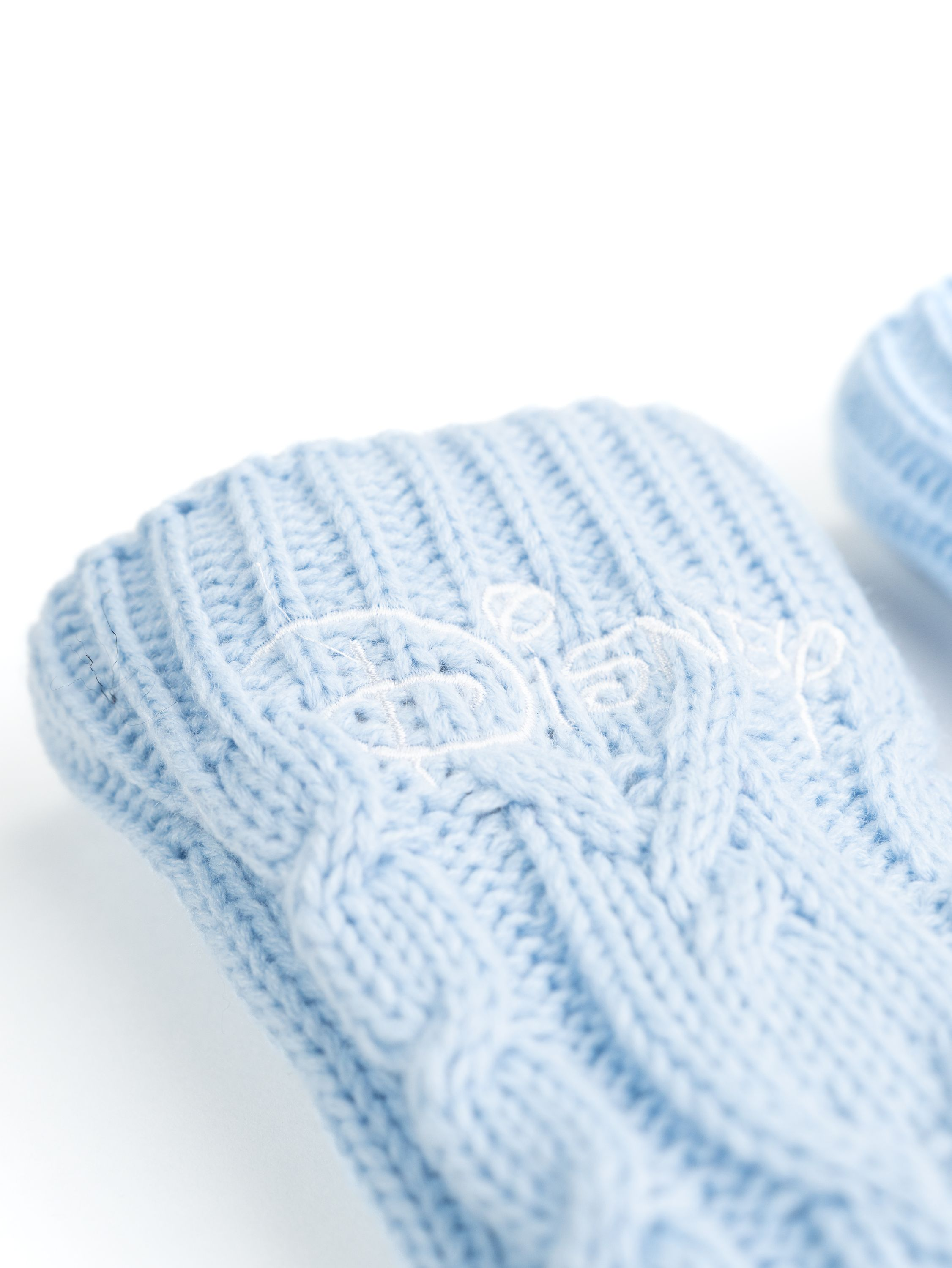 Nahaufnahme von hellblauen Strickhandschuhen mit dem Disney-Logo auf dem Bündchen gestickt. Weißer Hintergrund.
