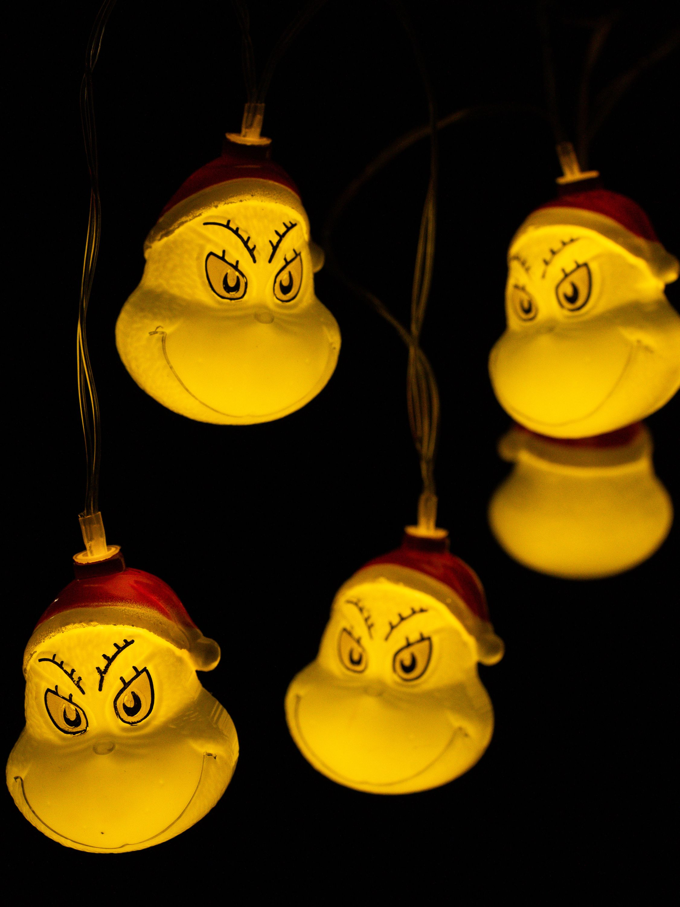 Lichterkette mit Grinch-ähnlichen Gesichtern auf schwarzem Hintergrund.