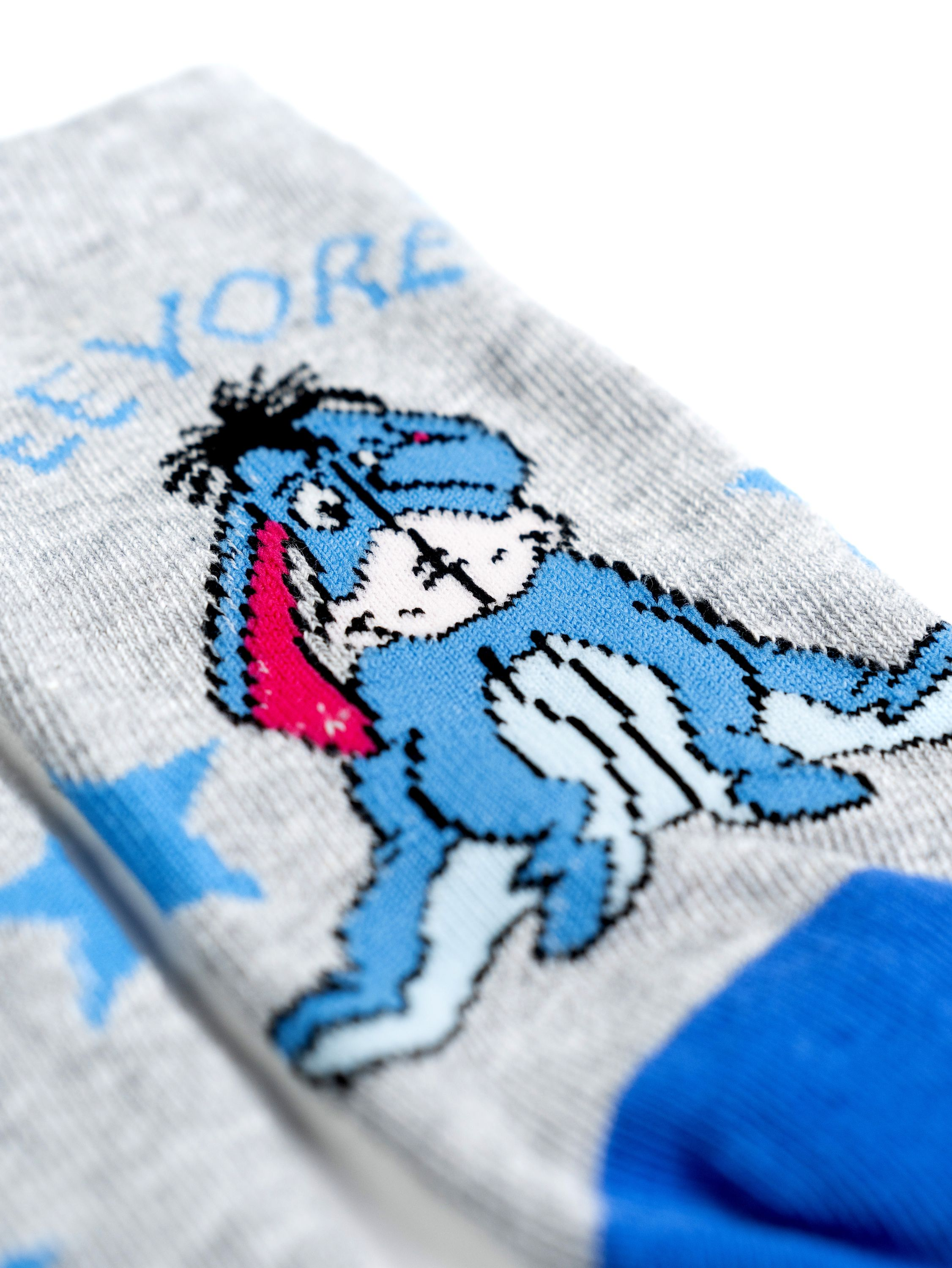 Nahaufnahme von grauen Socken mit I-Aah aus Winnie Puuh. Blaue Sterne und ein blau-weiß gestreifter Bund.