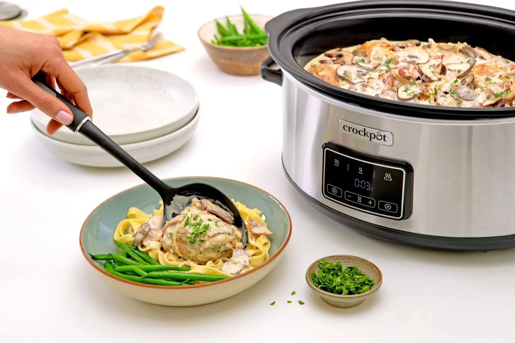 Una persona che serve cibo da una Crock-Pot con un mestolo, accompagnato da contorni.