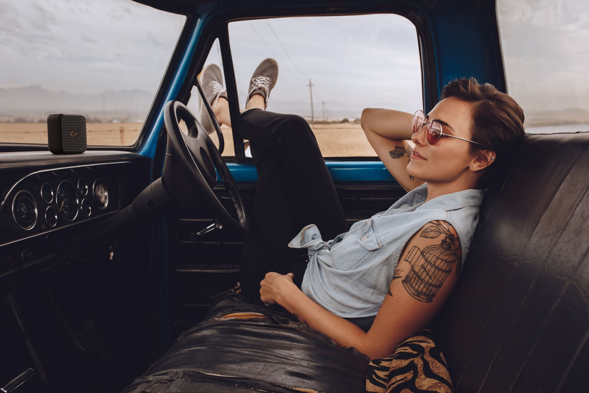 Vrouw ontspant in een vintage truck, luisterend naar een zwarte draagbare speaker.