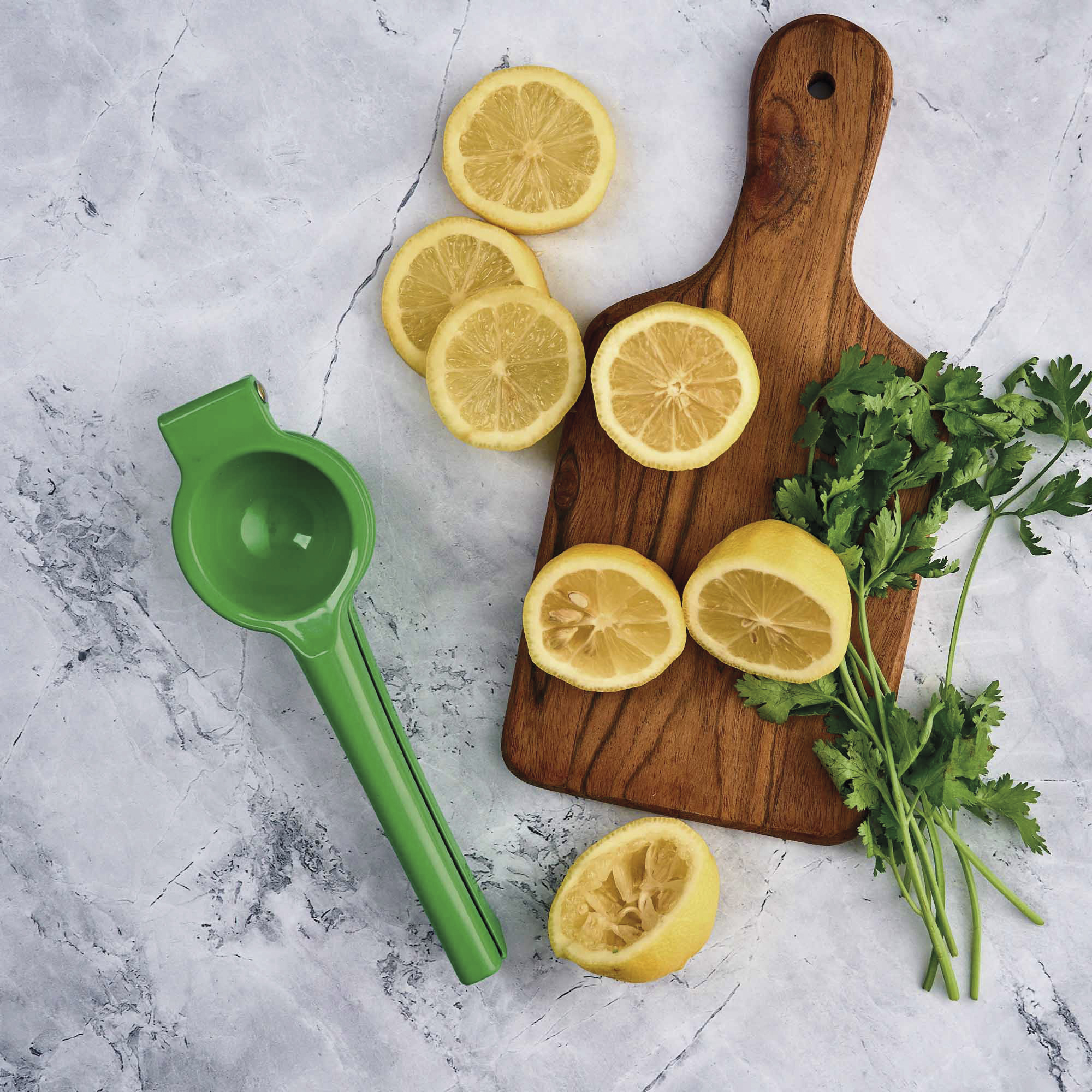 Limones, tabla de cortar, perejil y exprimidor verde sobre mármol. Vista cenital.