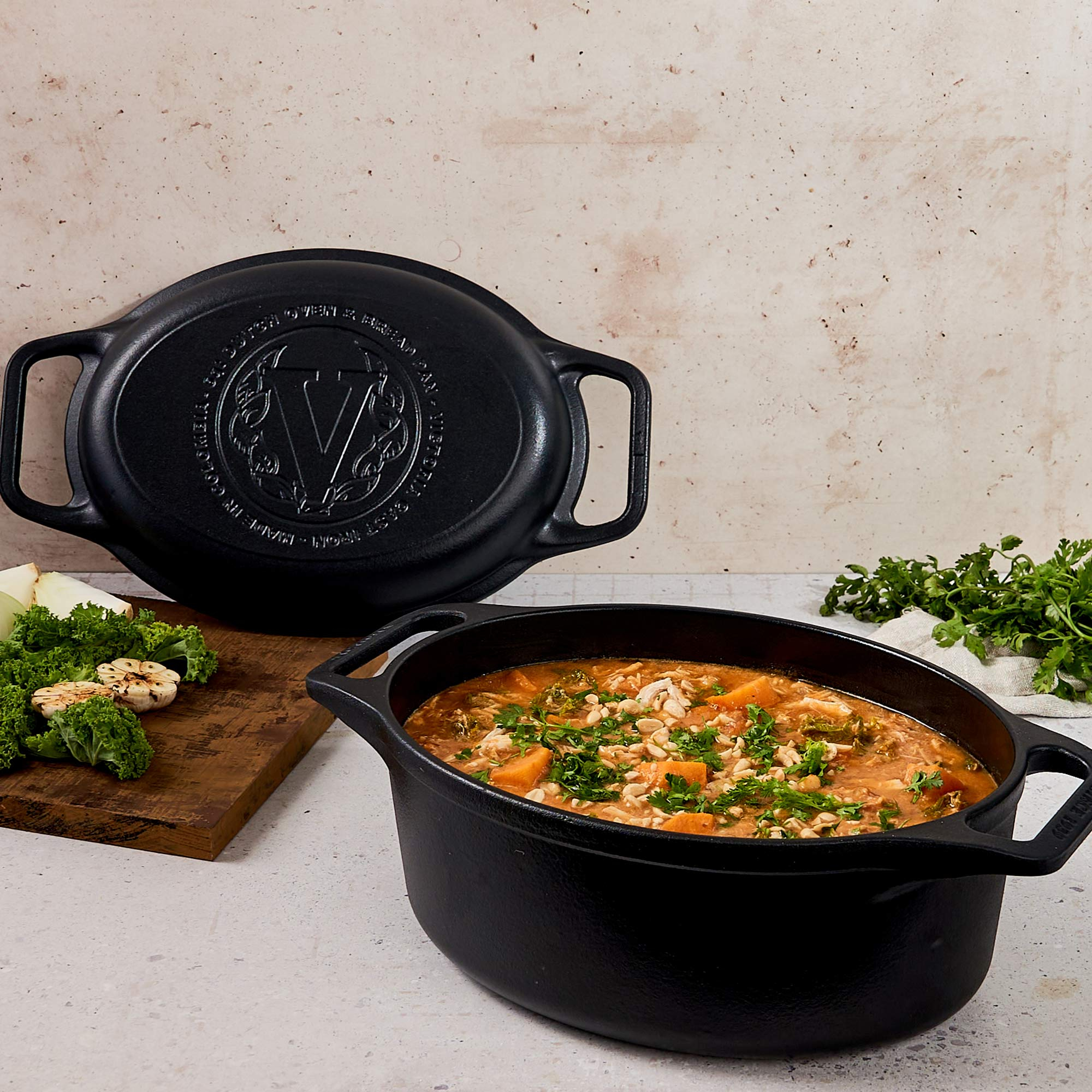Dos ollas ovaladas de hierro fundido negro. Una tapa encima, la otra olla contiene guiso con verduras y hierbas.