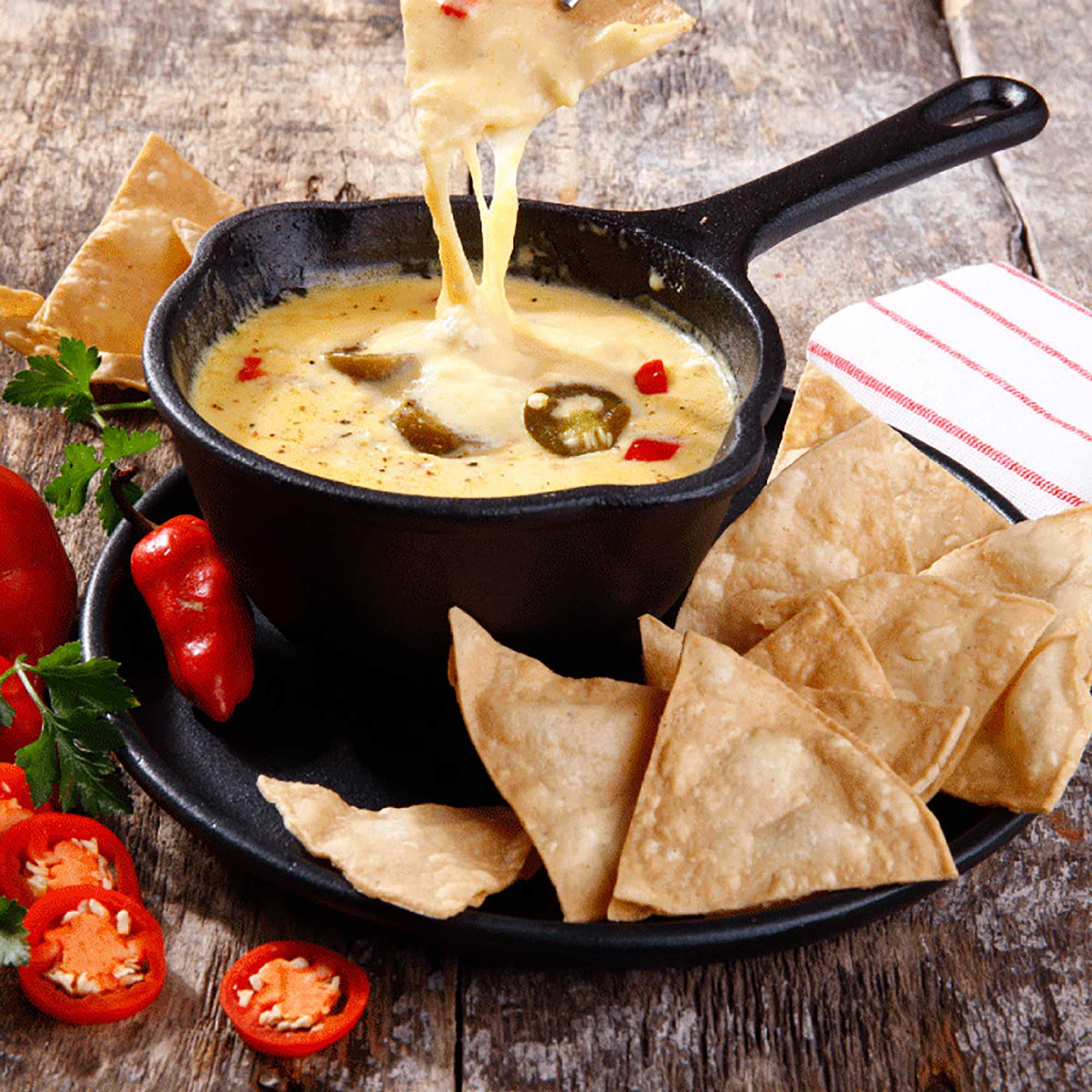 Dip de queso con jalapeños, servido con totopos. Caliente, cremoso y apetitoso, en mesa de madera.