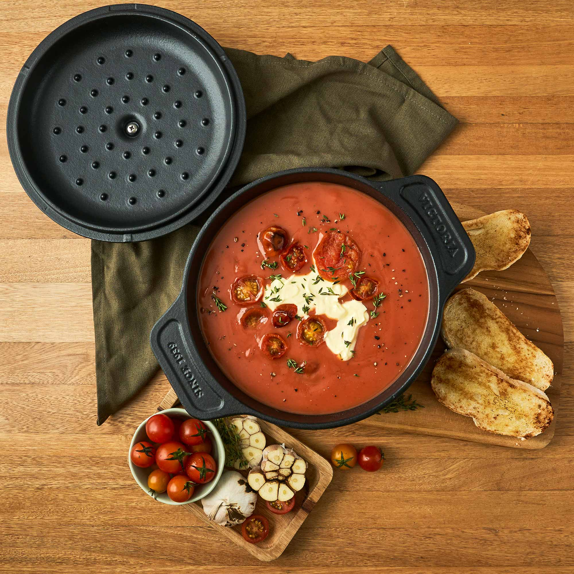 Vista aérea de sopa de tomate en una olla de hierro fundido negra, con pan e ingredientes.