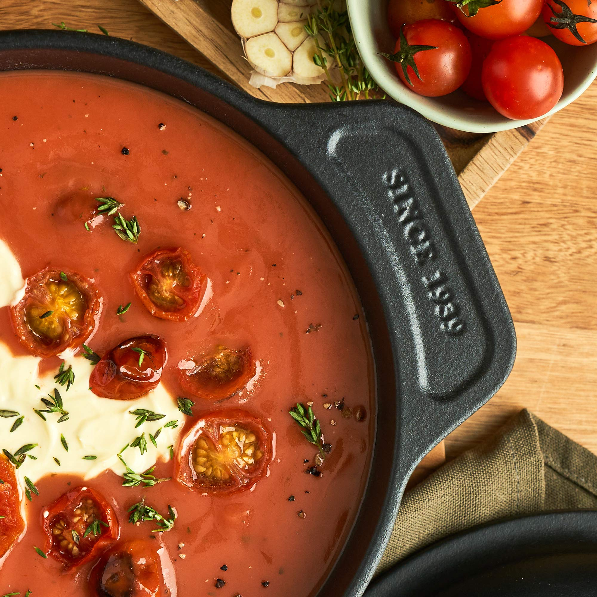 Sopa de tomate con tomates cherry y hierbas en una sartén de hierro fundido negro sobre madera.