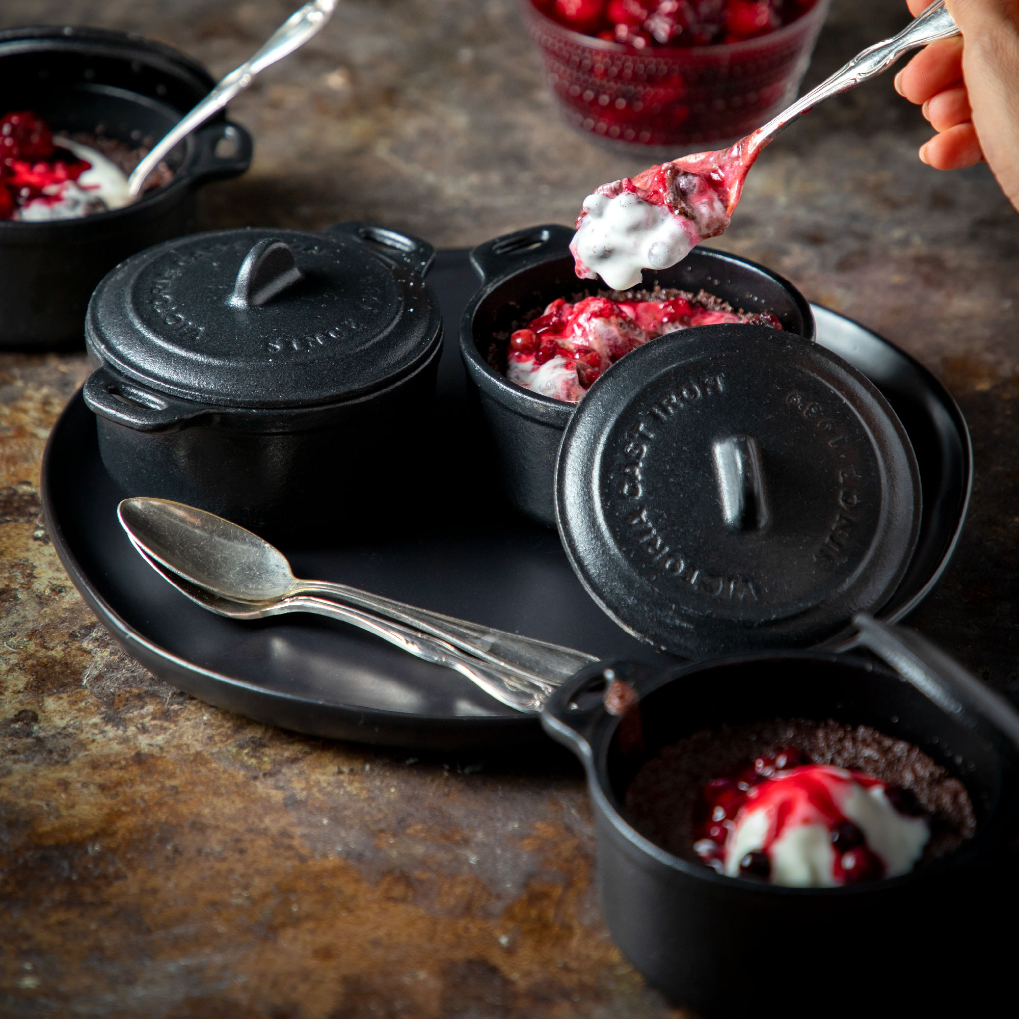 Ollas negras de hierro fundido con postres, cubiertos con bayas y crema batida.