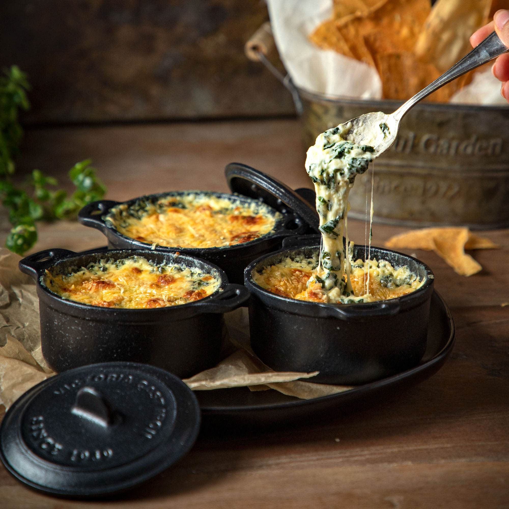 Tres platos negros con salsa de espinacas, una cuchara con queso y patatas fritas en un cubo.