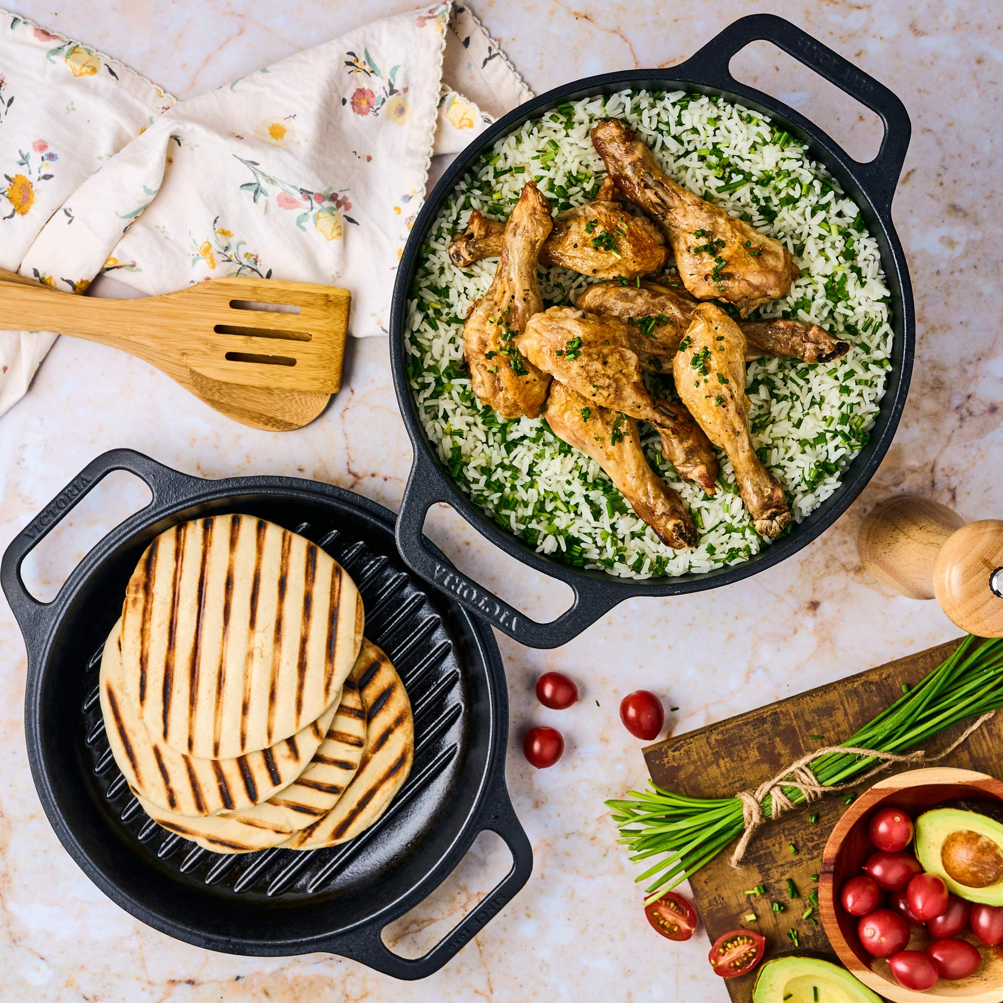 Vista aérea de una sartén de hierro fundido con pollo y arroz, otra con pan a la parrilla e ingredientes.
