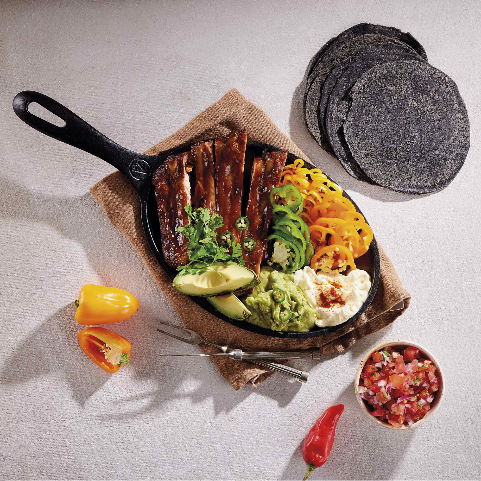Pfanne mit Rippchen, Tortillas, Guacamole, Paprika und Salsa. Draufsicht.