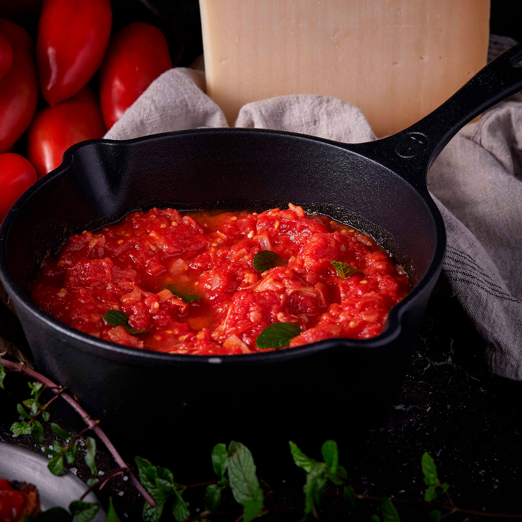 Sartén de hierro fundido con salsa de tomate, hierbas frescas y queso en el fondo.