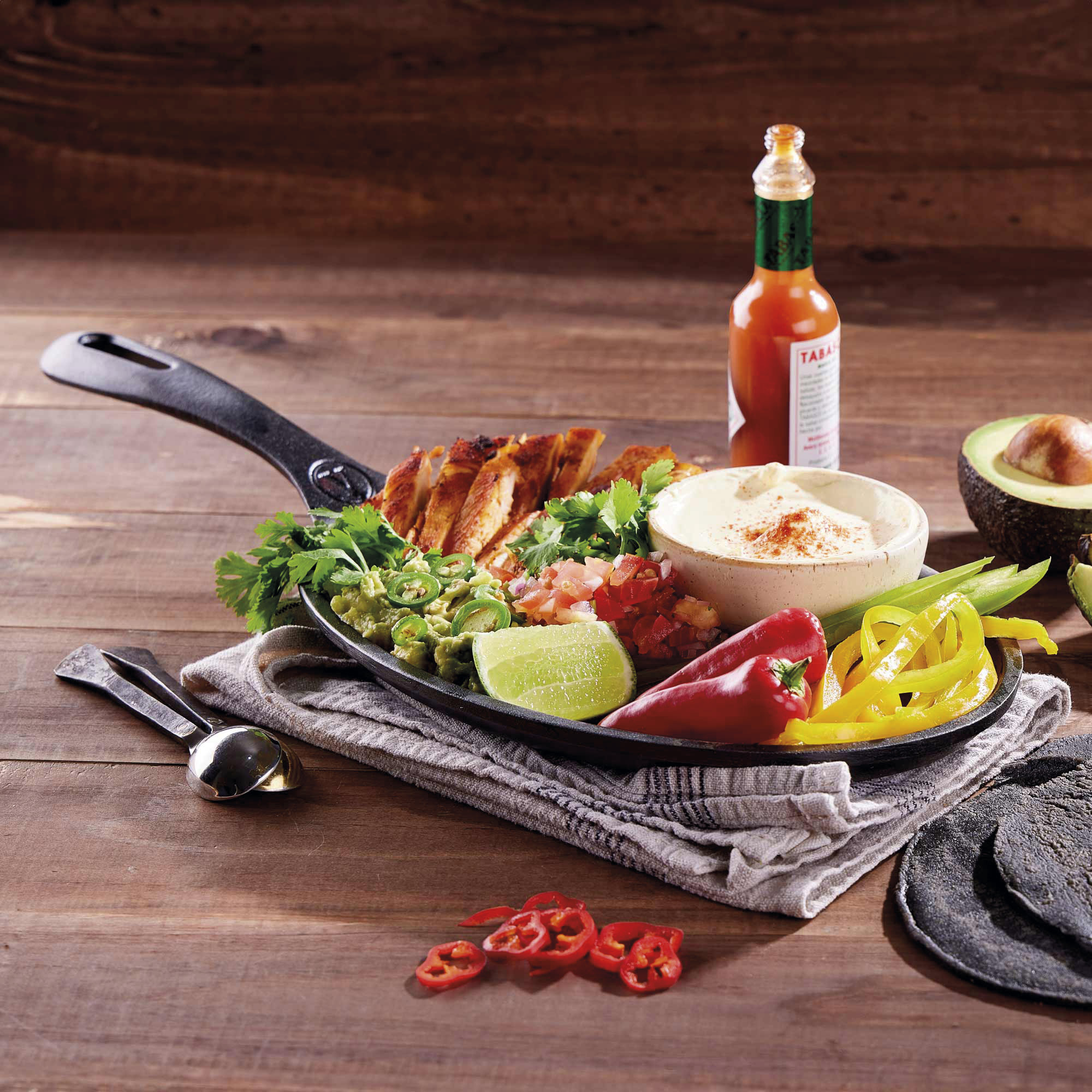 Fajita-Mahlzeit auf einer Bratpfanne, mit Hühnchen, Guacamole, Salsa und Paprika auf Holztisch.