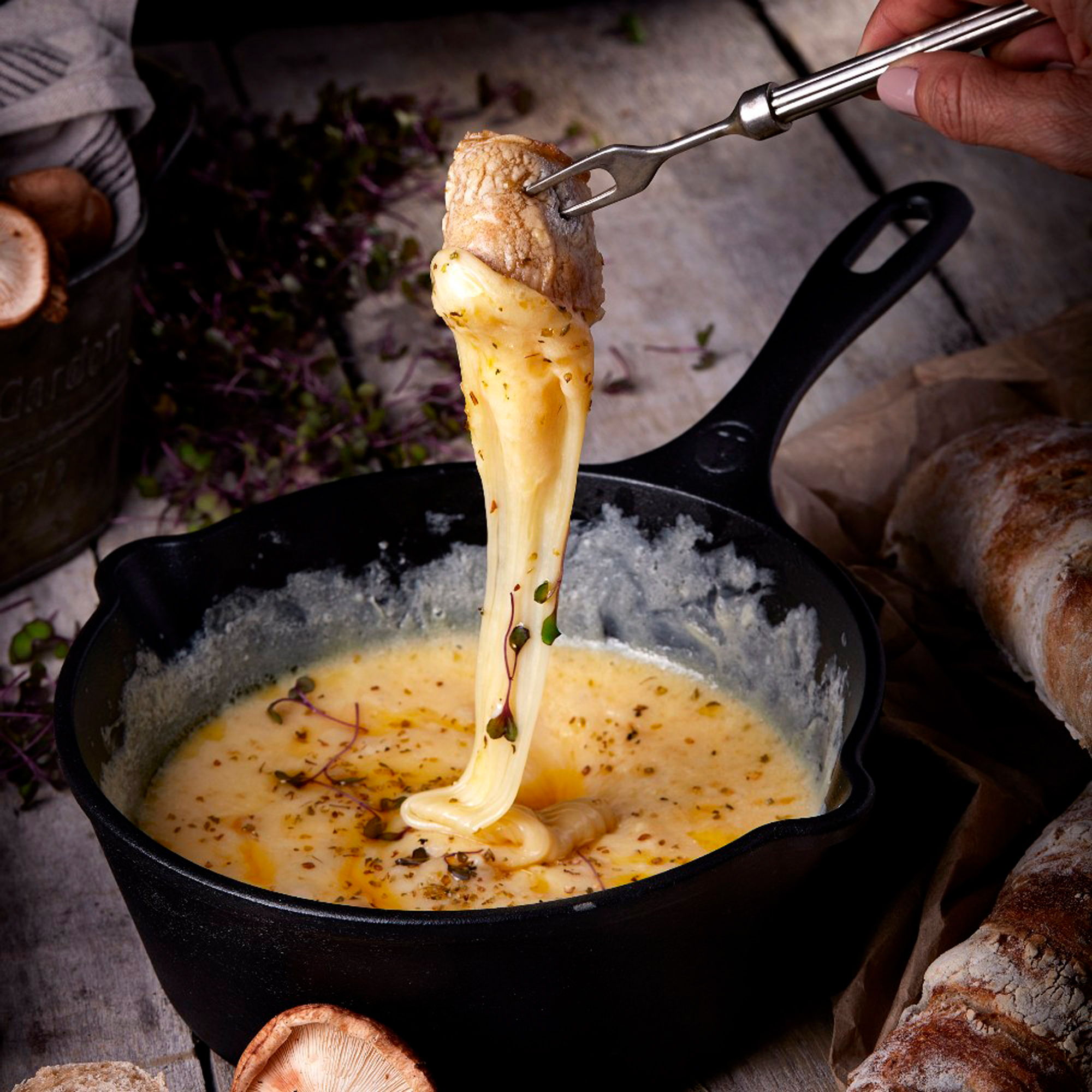 Un tenedor levanta queso de una sartén de queso derretido con pan y champiñones.