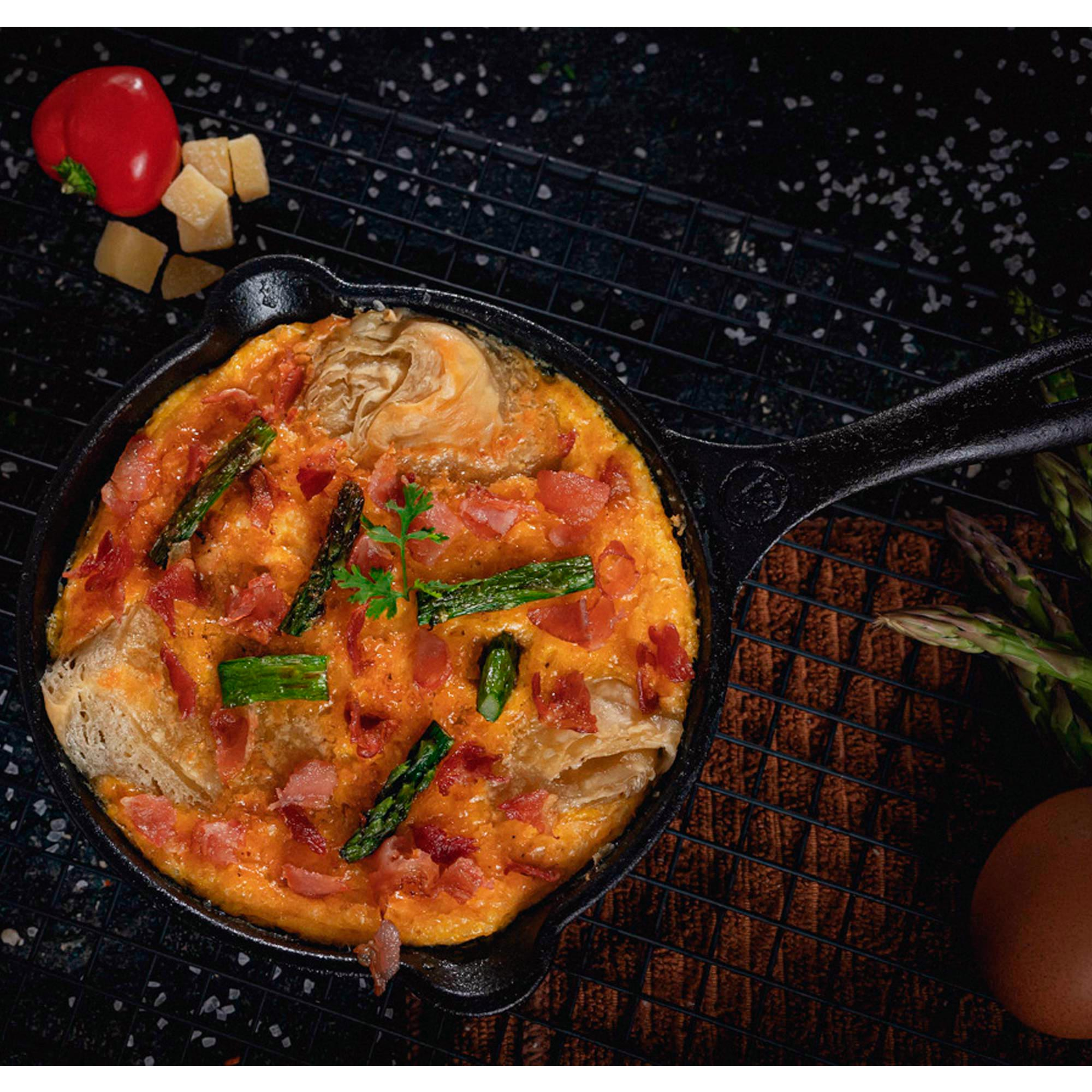 Omelett in einer Eisenpfanne mit Spargel, Schinken und Käse. Roter Pfeffer und Käsewürfel.