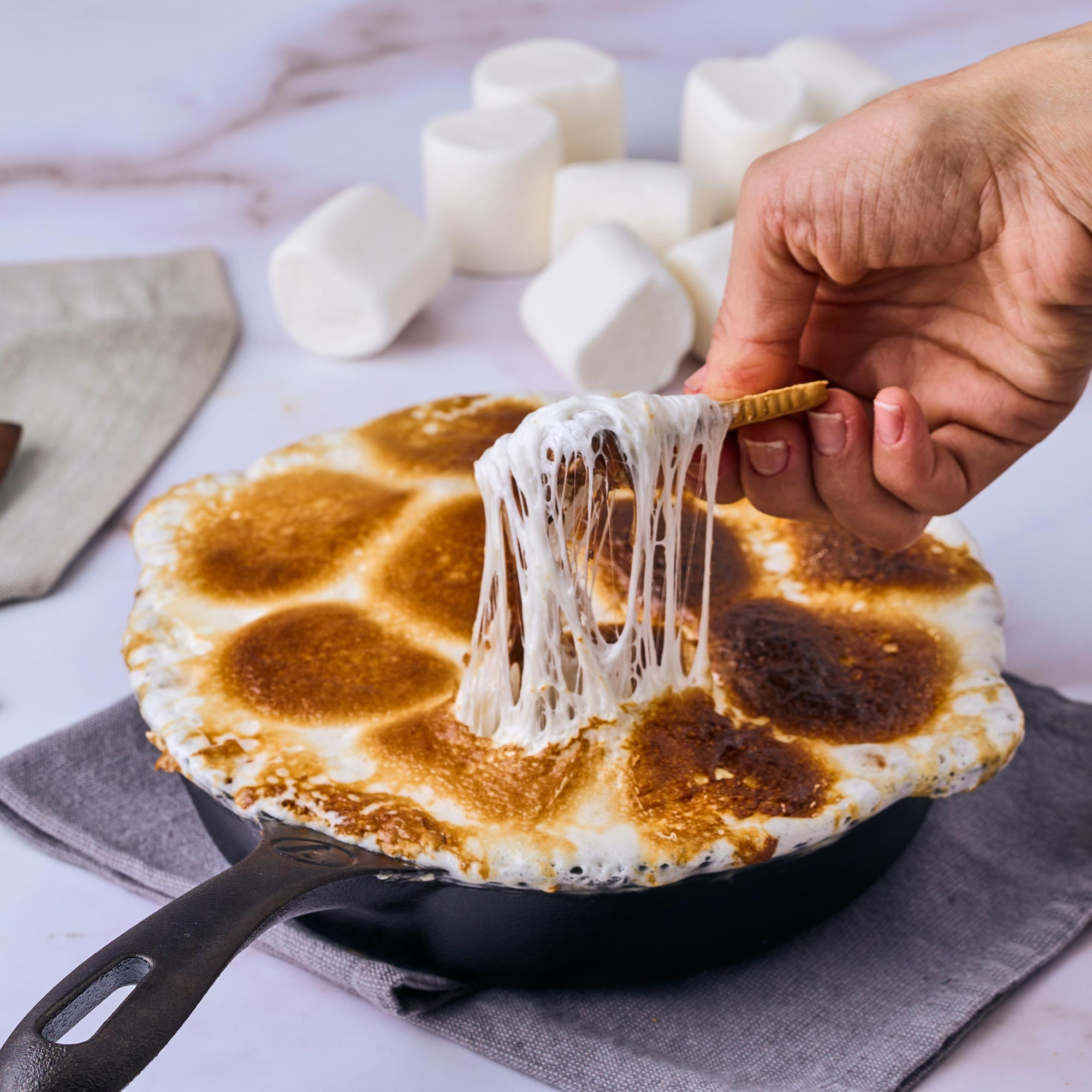 S'mores in einer Gusseisenpfanne, mit geschmolzenem Marshmallow, das von einem Cracker hochgezogen wird.