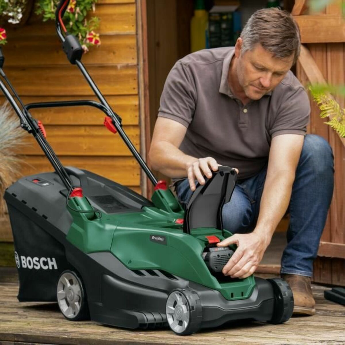Mann, der einen grün-schwarzen Bosch Rasenmäher im Freien benutzt. Er stellt die Batterie ein.