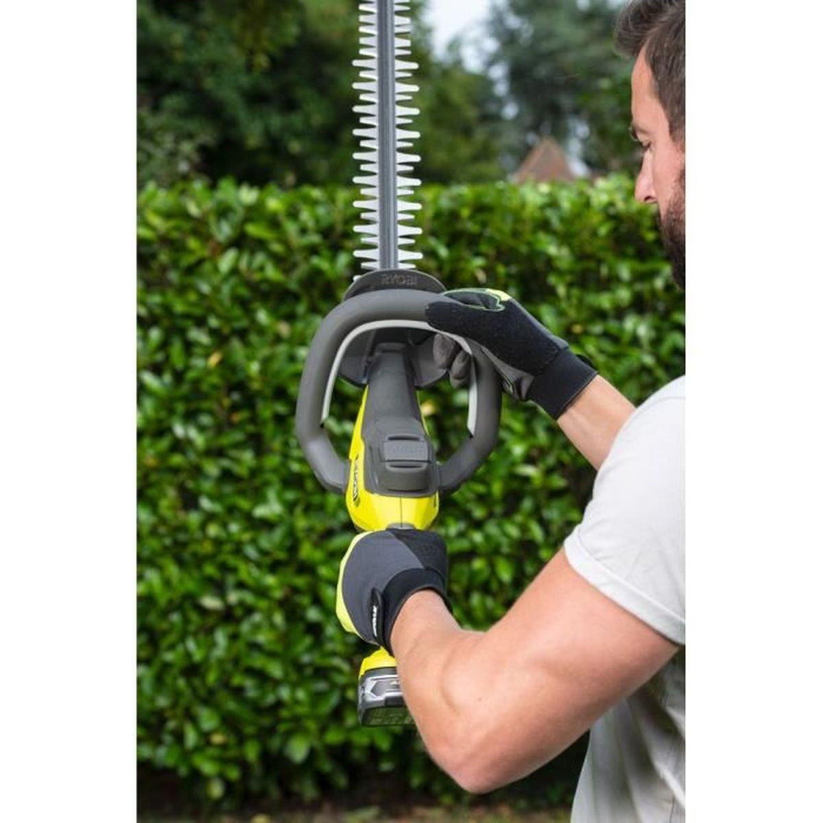 Eine Person benutzt eine grün-gelbe Heckenschere. Sie trägt Handschuhe und schaut sich das Werkzeug an.