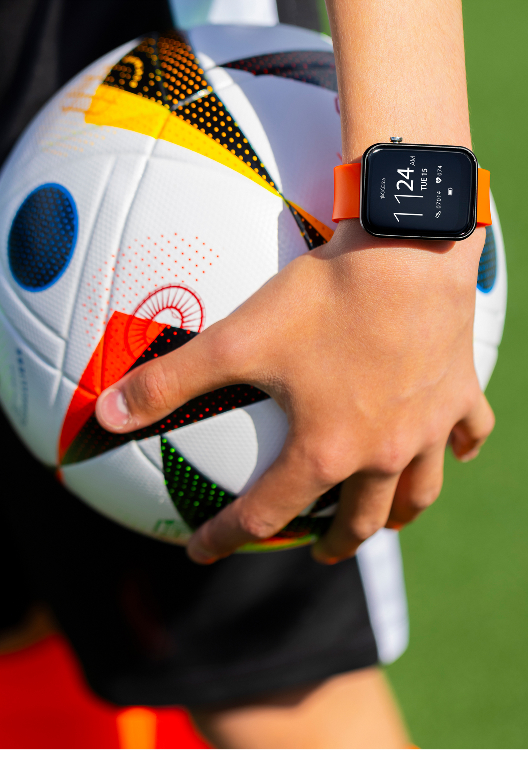 Ein Arm hält einen Fußball, trägt eine Uhr mit orangefarbenem Armband.