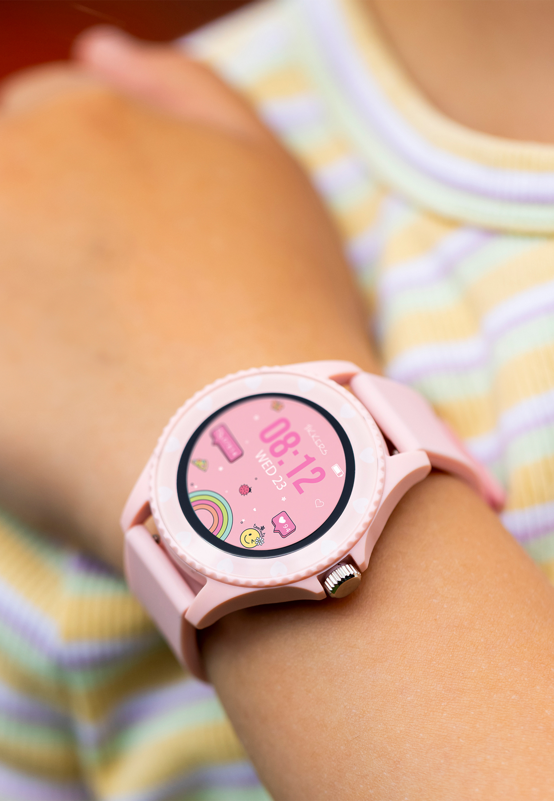 Le poignet d'un enfant avec une smartwatch rose affichant l'heure et quelques icônes.