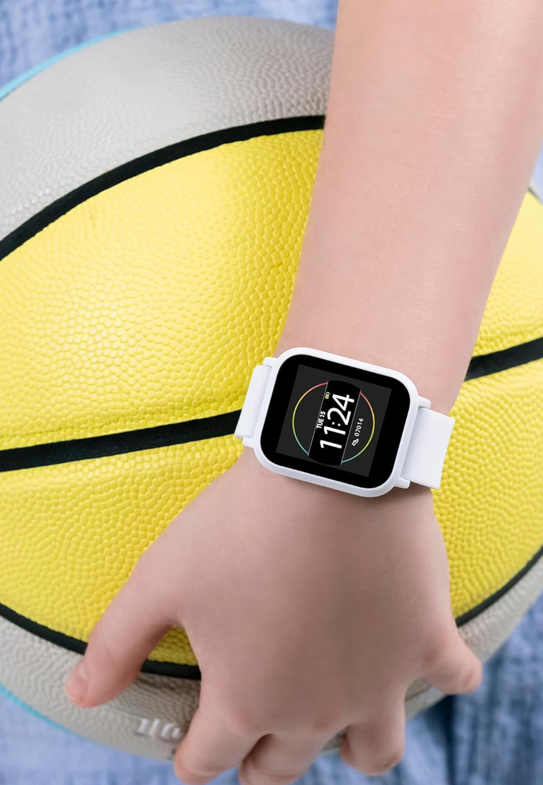 La mano di un bambino tiene un pallone da basket giallo. Uno smartwatch bianco mostra l'ora.