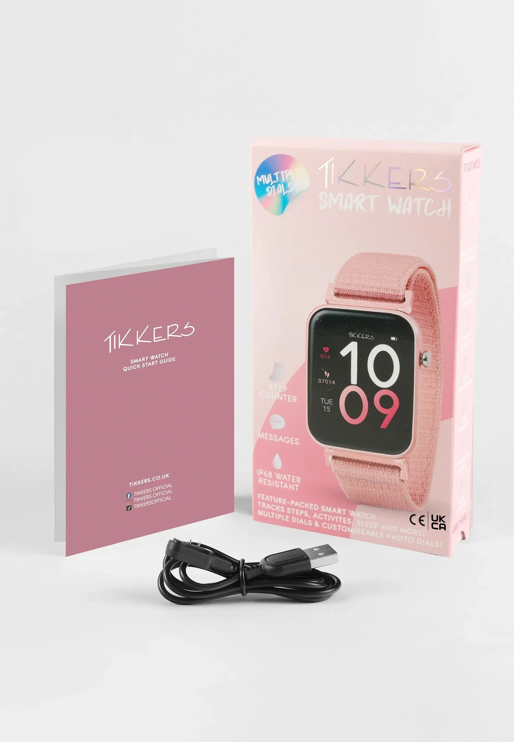Une montre intelligente rose, une boîte et un manuel sont sur une surface blanche. Un câble de charge est en dessous.