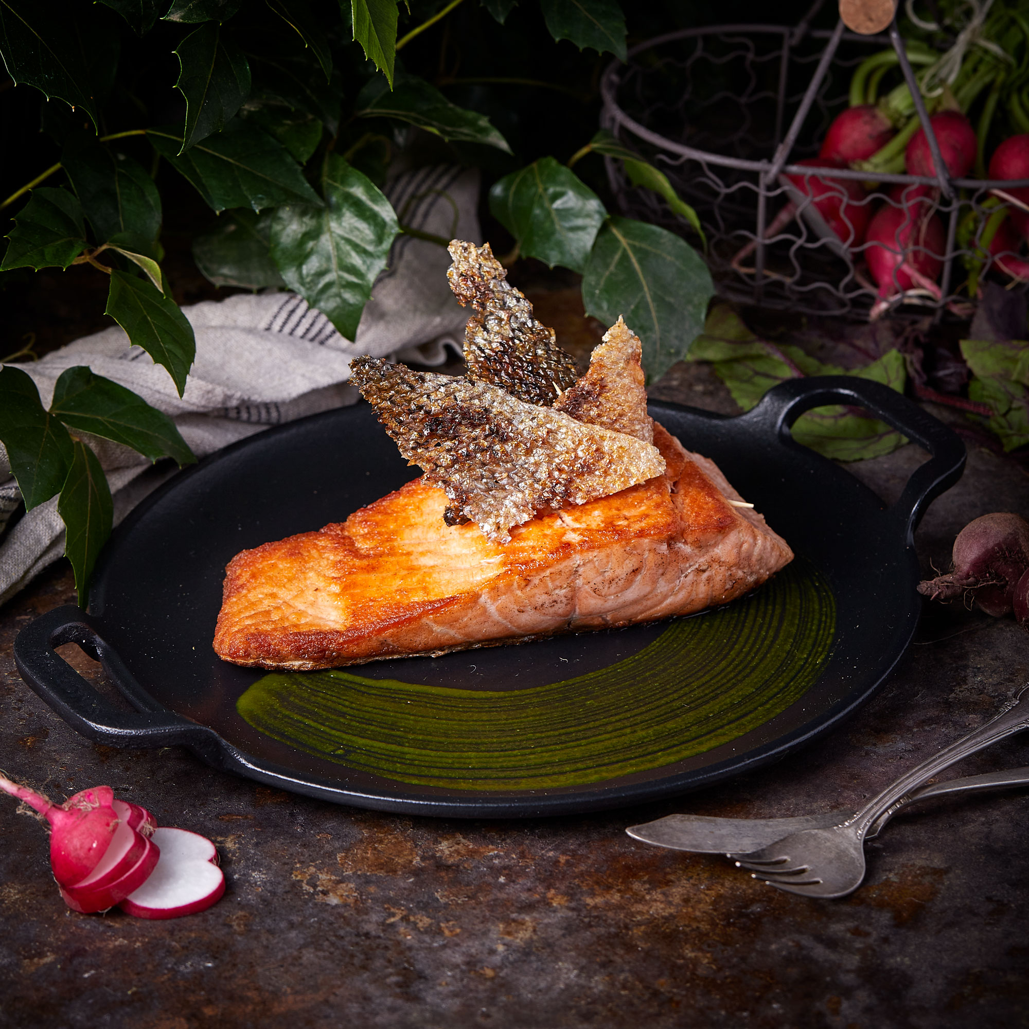 Gegrillter Lachs auf einem schwarzen Teller mit grüner Sauce, mit knuspriger Haut garniert.