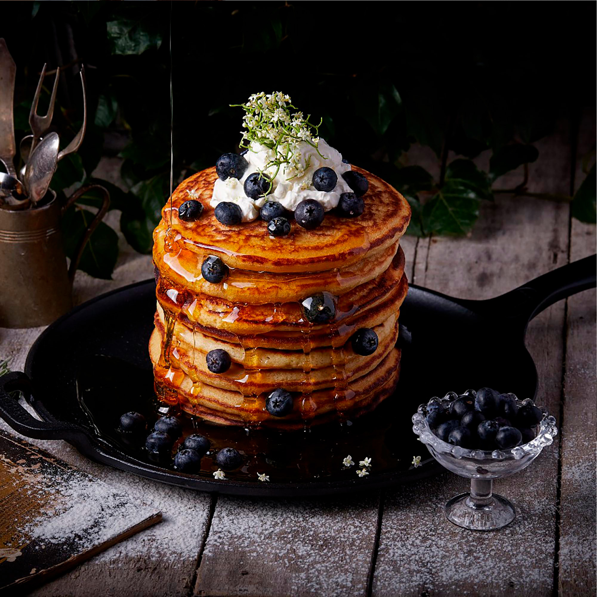 Pfannkuchenstapel mit Blaubeeren, Schlagsahne und Honig. Serviert auf einem schwarzen Teller mit Sirup.