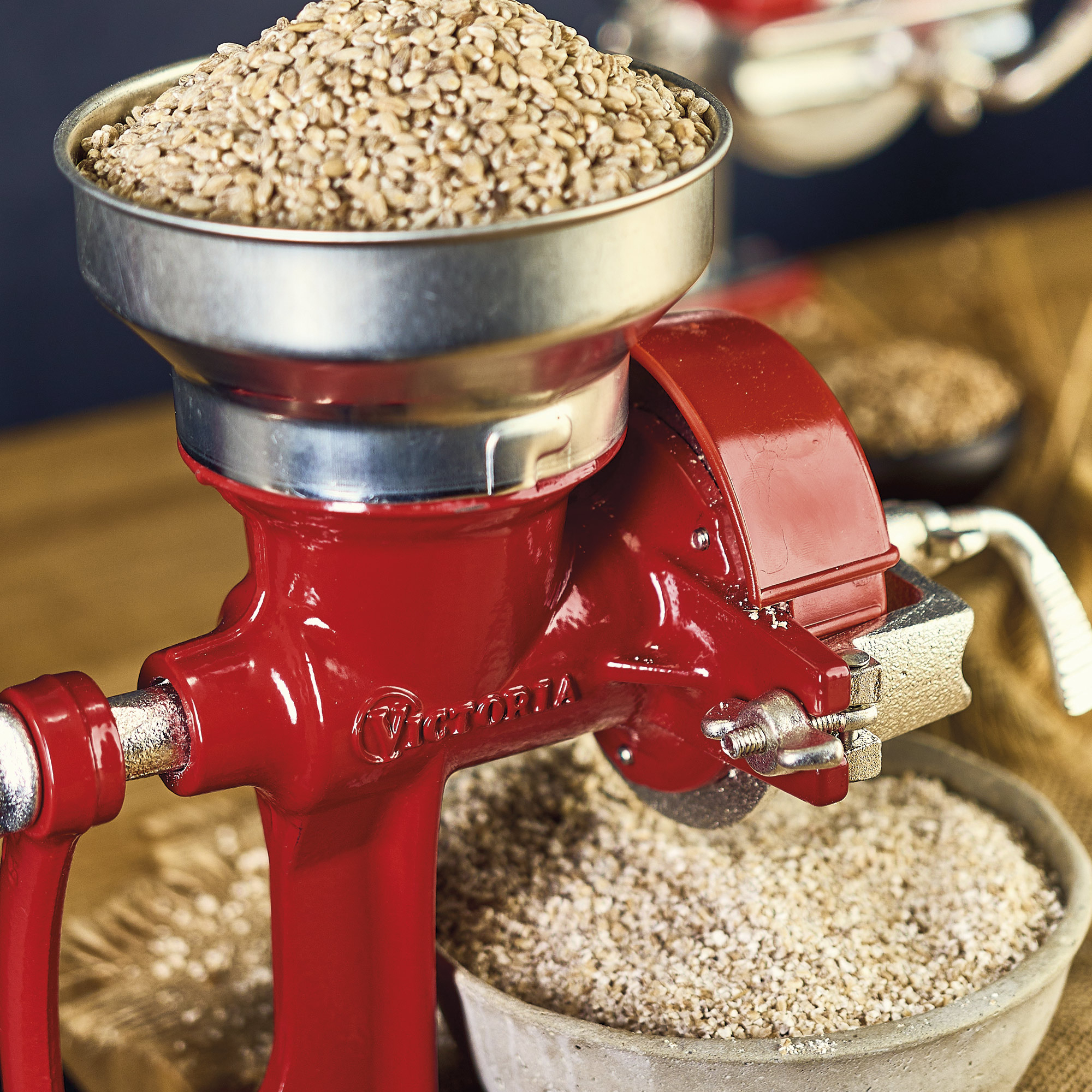 Eine rote Getreidemühle mit einer Silberschüssel, die Getreide enthält. Eine zweite Schüssel enthält mehr Getreide.