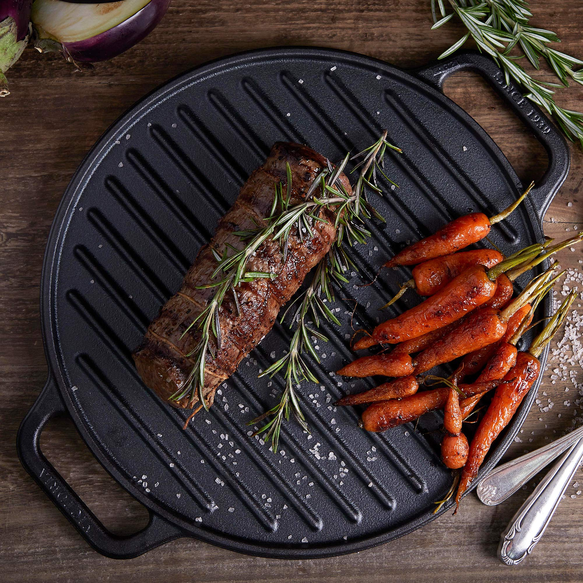 Gegrilltes Fleisch und Karotten auf einer schwarzen Grillpfanne.