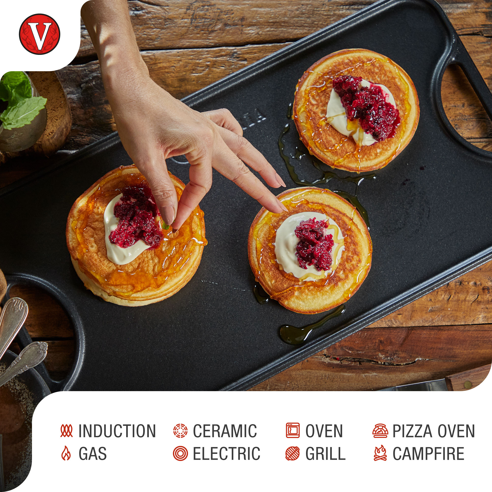 Pfannkuchen mit Schlagsahne und Beeren belegt, mit Sirup beträufelt, auf einer schwarzen Grillplatte.