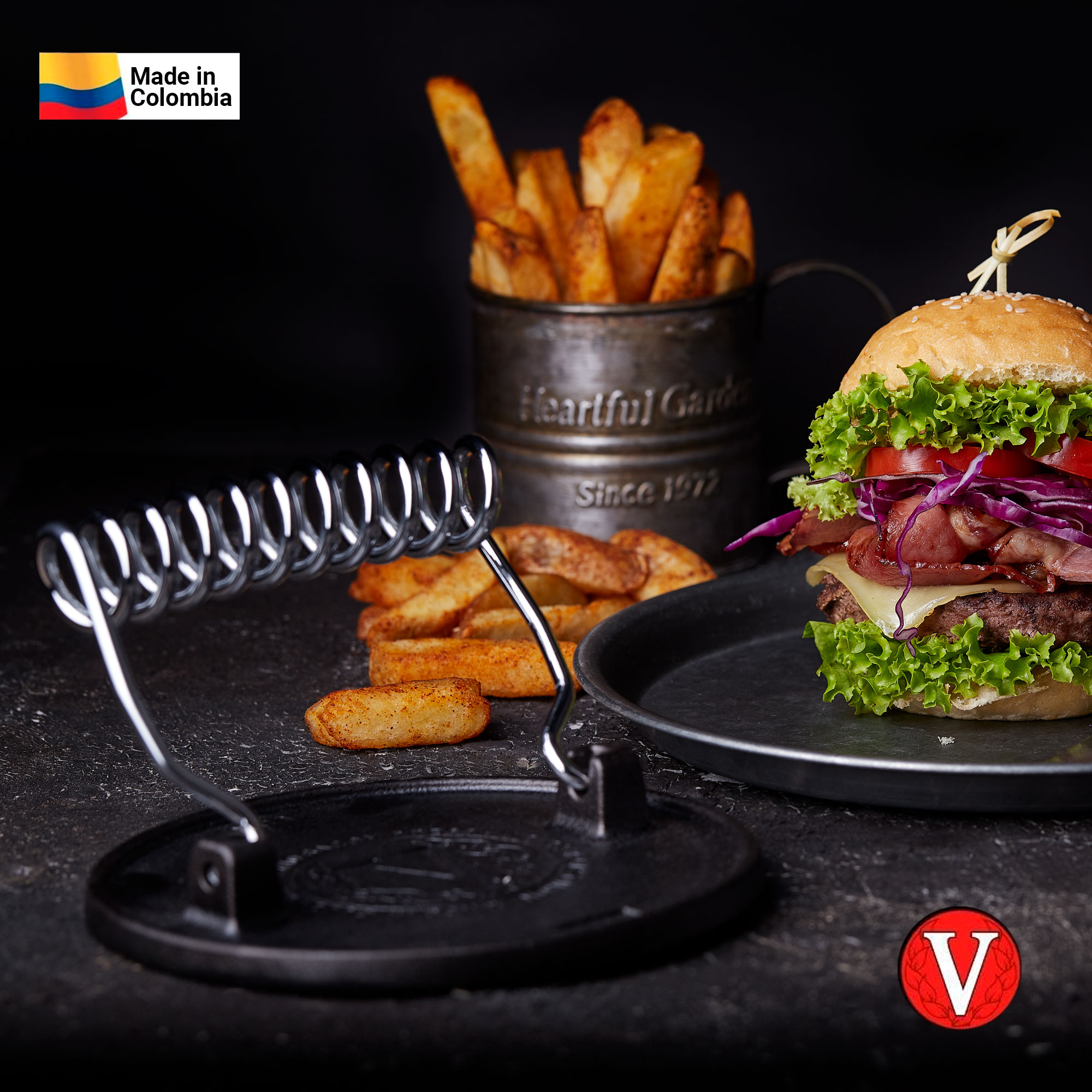 Hamburguesa con papas fritas y soporte. Fondo negro. Logotipo 'Made in Colombia'.