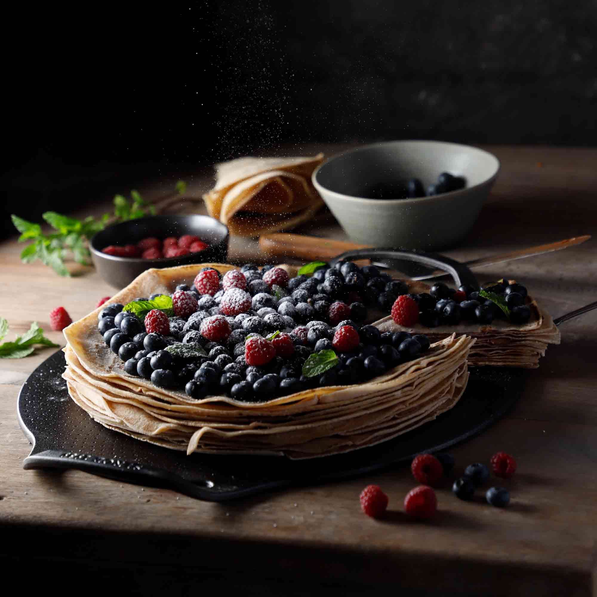 Pfannkuchen mit Blaubeeren und Himbeeren, mit Puderzucker bestreut. Dunkler Hintergrund.
