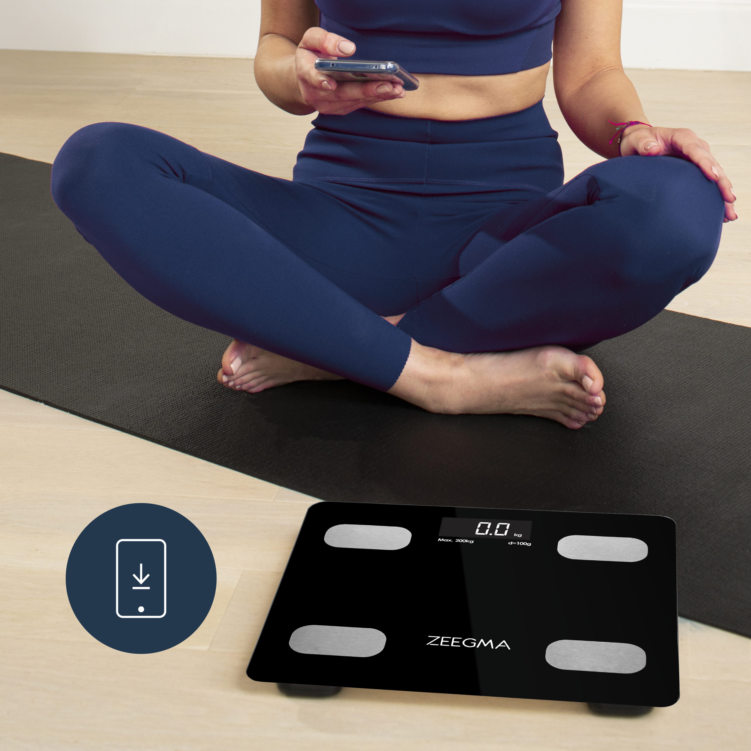 Kobieta siedzi na macie do jogi, z wagą cyfrową. Używa telefonu. Waga ma ekran.