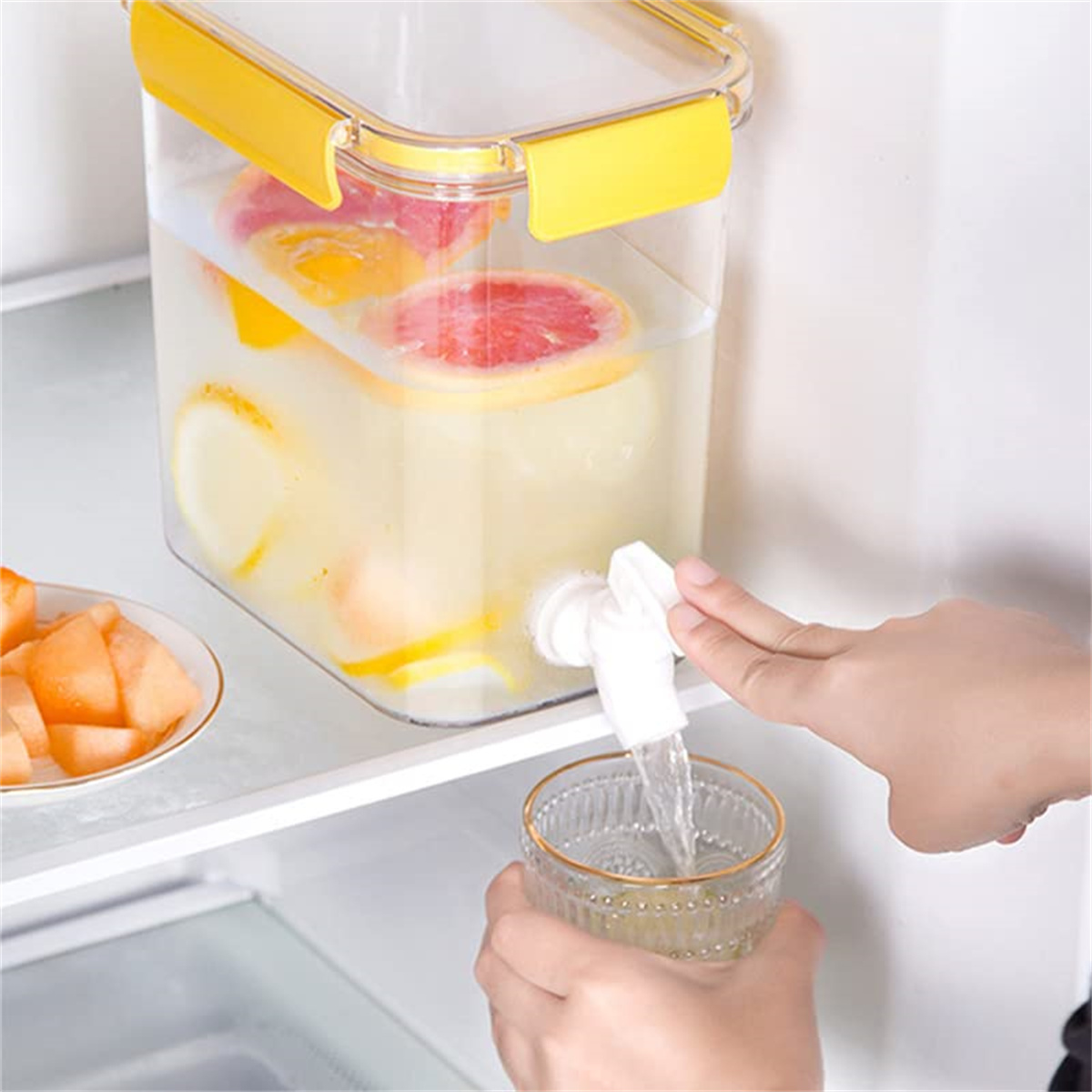 Eine Person gießt Wasser mit Zitrusfrüchten aus einem Spender in einem Kühlschrank in ein Glas.