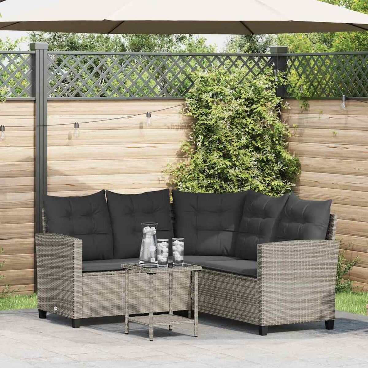 Graues Ecksofa-Set aus Rattan mit Kissen und Tisch. Draußen unter Sonnenschirm und Zaun.