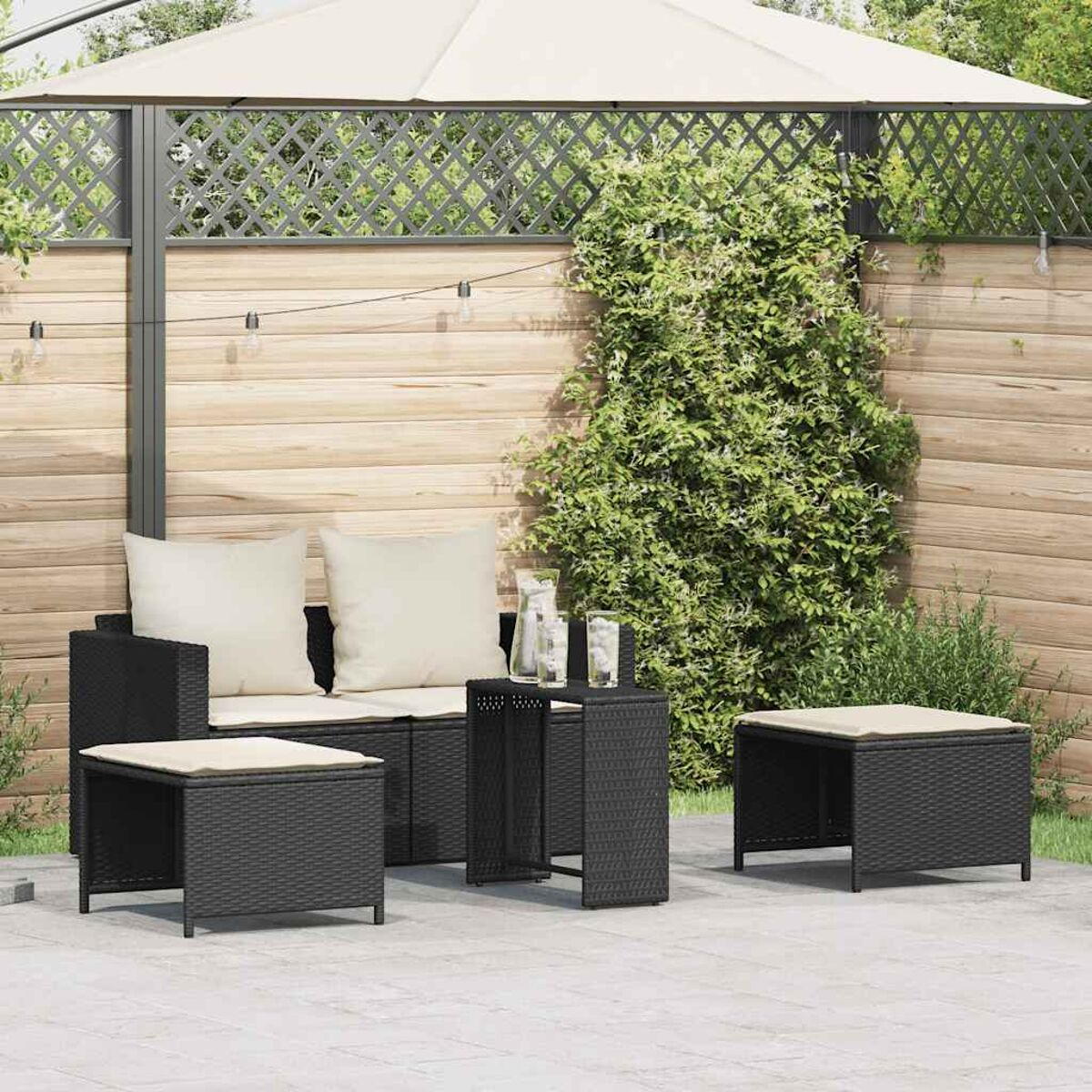 Set di mobili da patio all'aperto: divano in vimini nero, tavolino e pouf con cuscini color crema.