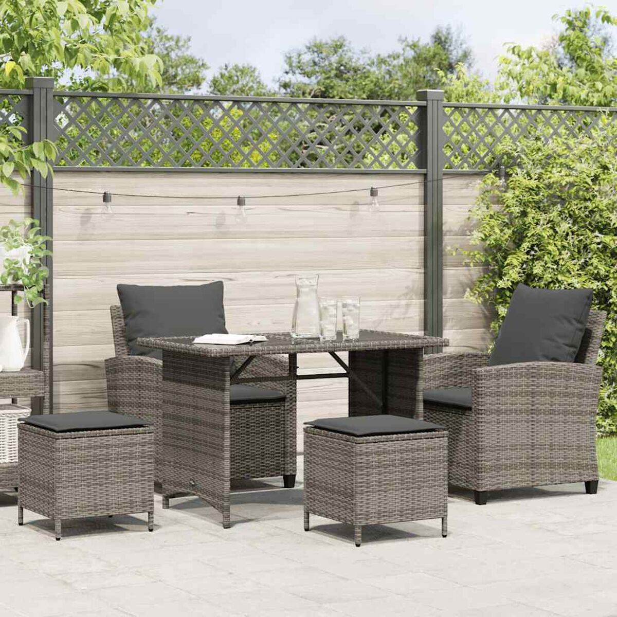 Set di mobili da patio: un tavolo, due sedie e due pouf. Vimini grigio con cuscini grigi, su un patio.