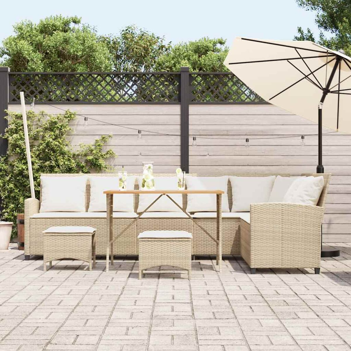 Set di mobili da esterno. Include un divano angolare, tavolo, sgabelli e un ombrellone. Vimini beige con cuscini bianchi. Ambiente soleggiato.