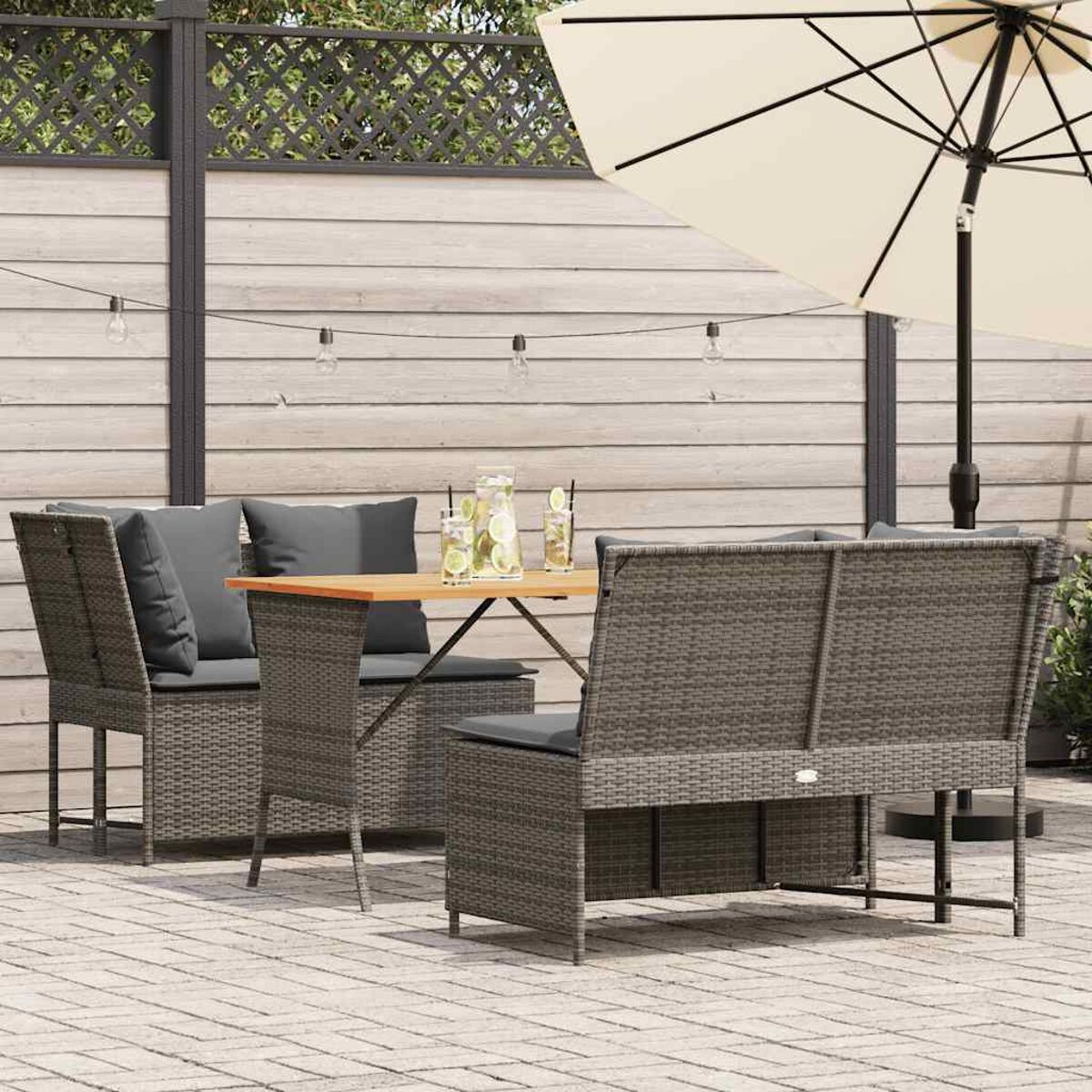 Set patio esterno. Mobili in vimini grigi, tavolo in legno, ombrellone e lucine.