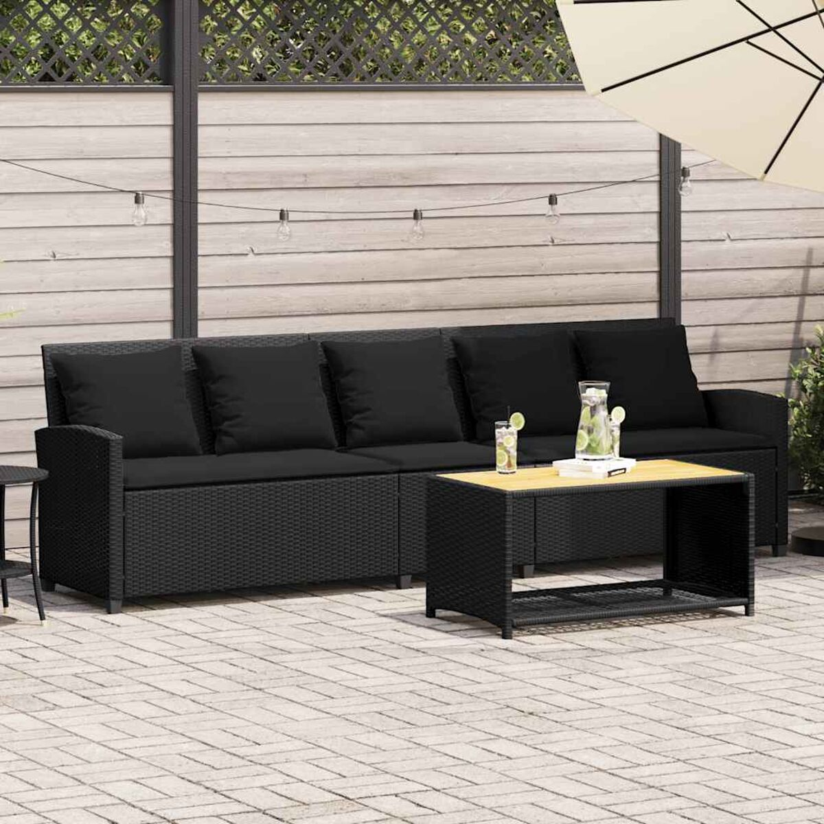 Set divano in rattan nero con tavolo, bevande e cuscini.