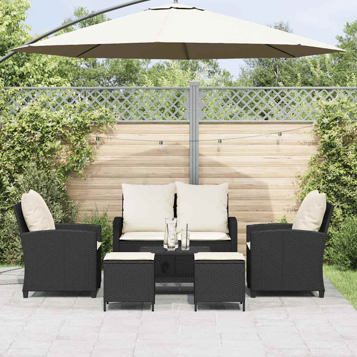Set patio esterno con mobili in vimini neri, include divano, due sedie e due pouf.