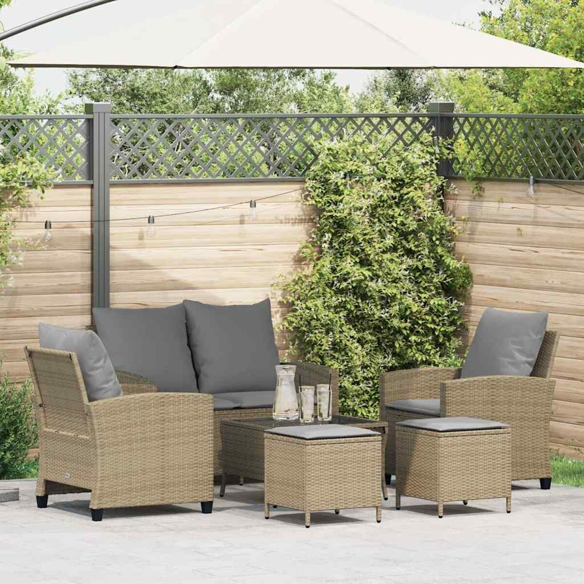 Set da patio esterno: divano in vimini, due poltrone, un tavolo e due pouf con cuscini grigi.