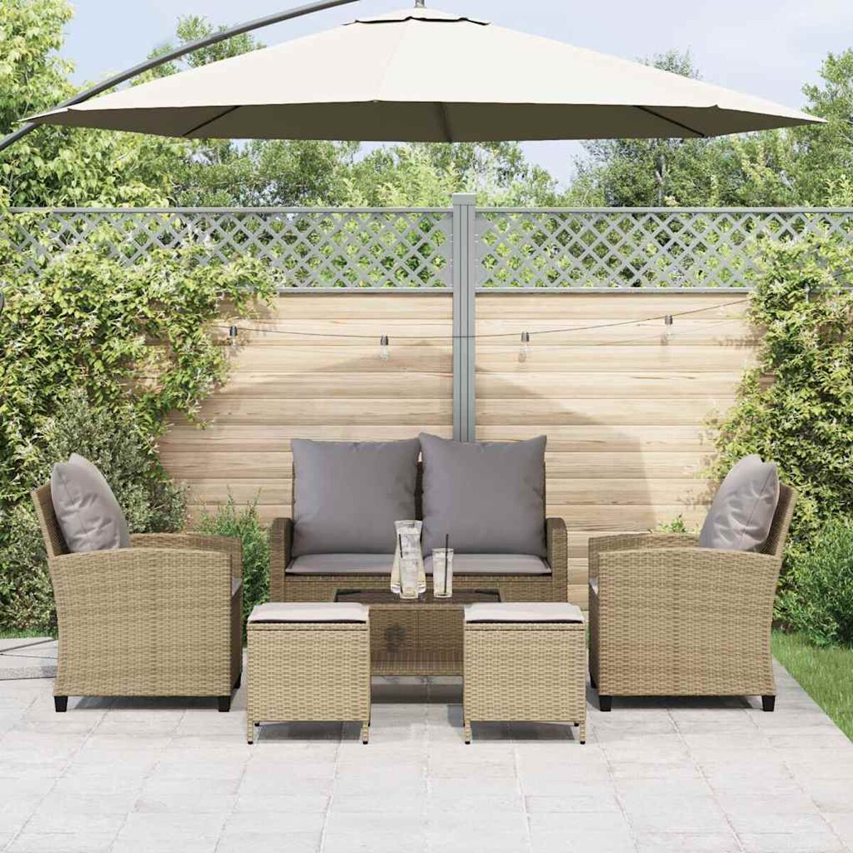 Set patio esterno con mobili in vimini beige, cuscini grigi, un tavolo di vetro e un grande ombrellone. Piante verdi.