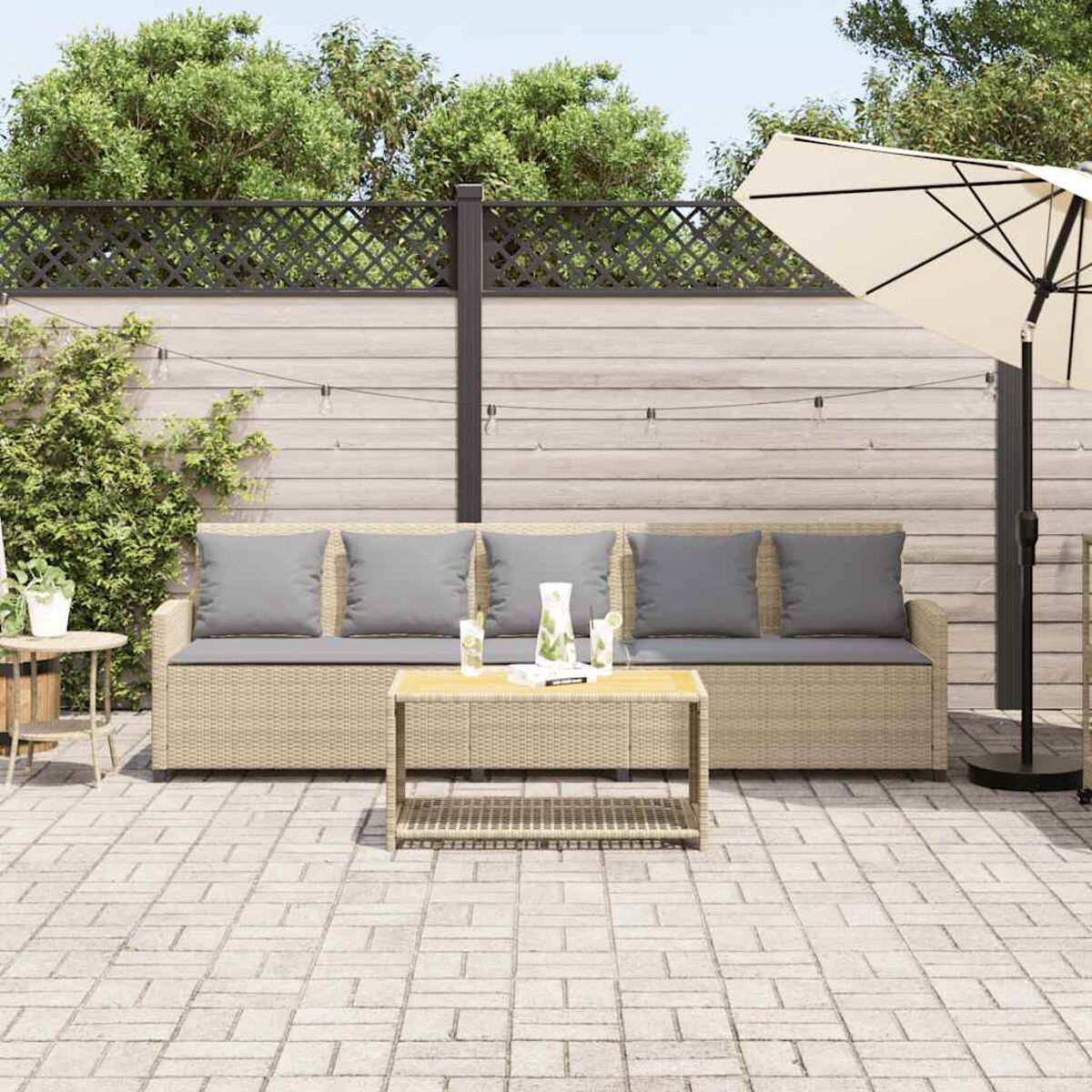 Set patio esterno con divano beige, cuscini grigi, tavolo e ombrellone. Pavimento in mattoni.