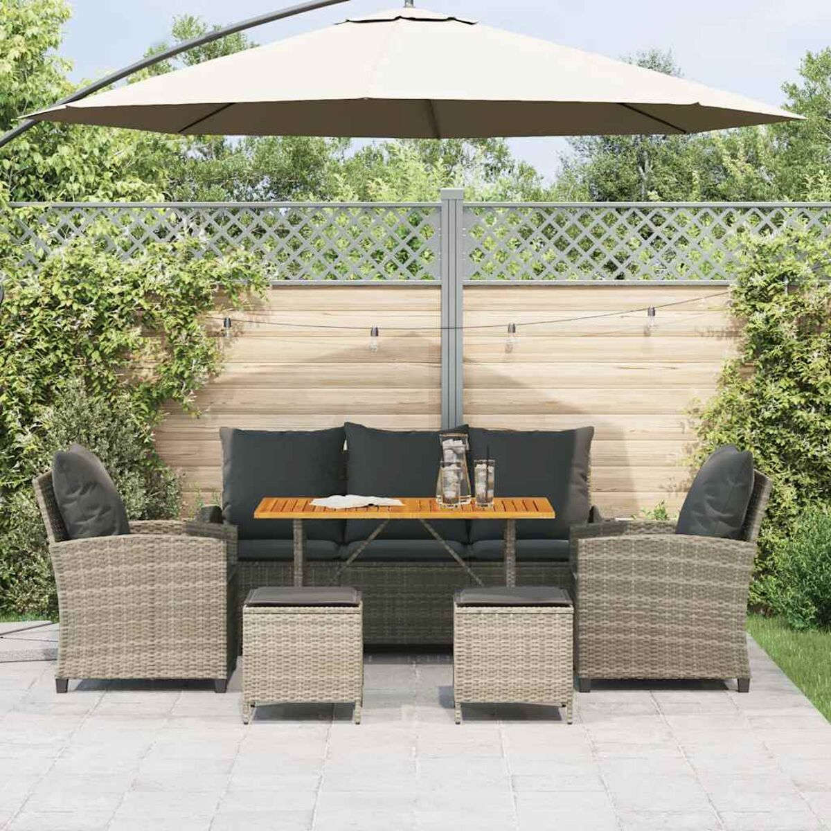 Gartenmöbel-Set aus Korbgeflecht im Garten. Sofa, Sessel und Fußstützen. Tisch, Sonnenschirm und Lichterketten.