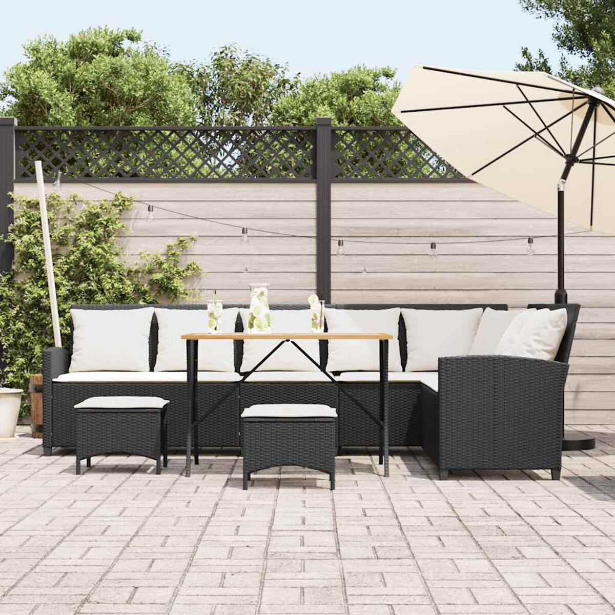Set da patio esterno con un divano in vimini nero, tavolo, sedie e ombrellone. La scena è soleggiata.