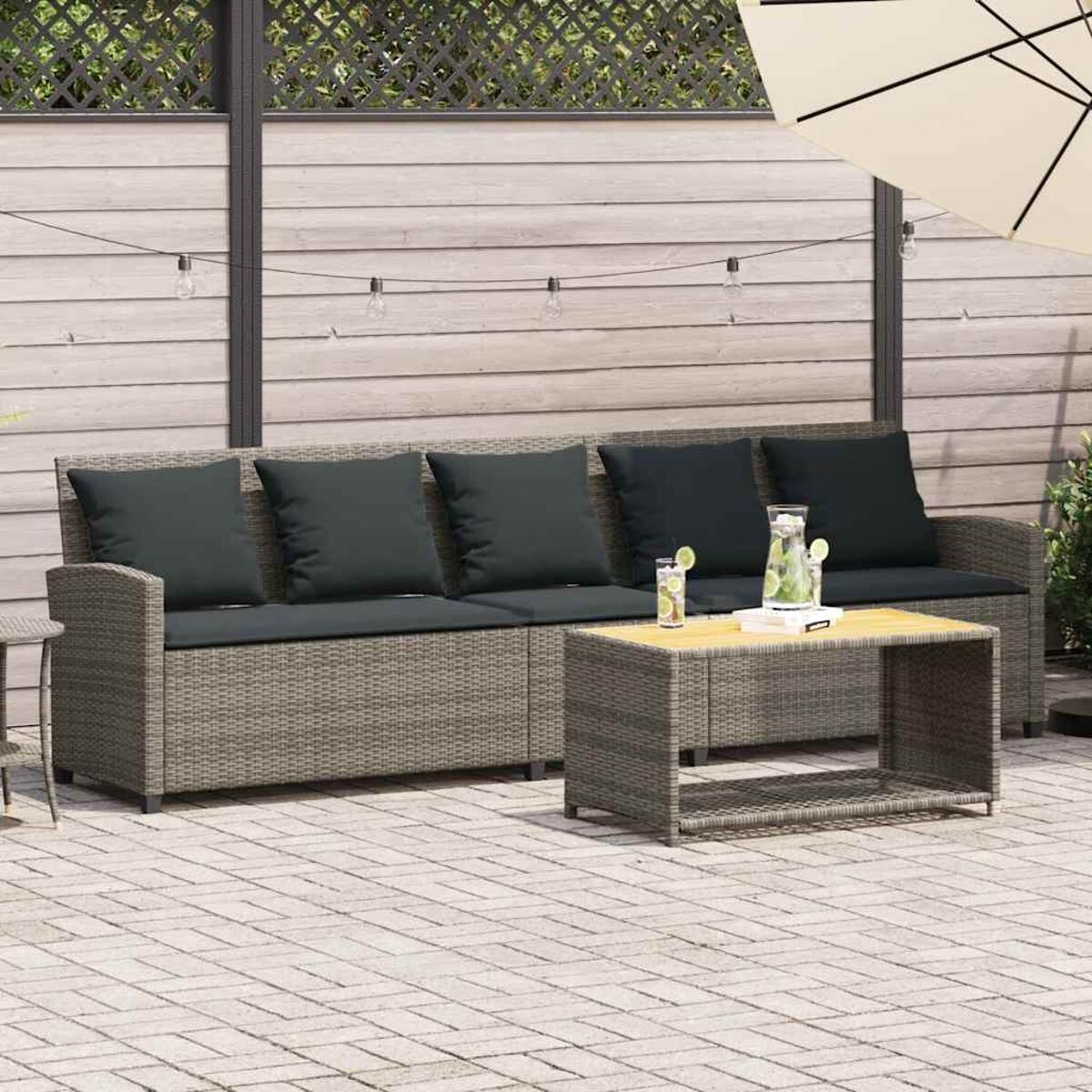 Set divano in vimini grigio con tavolino e cuscini. Su un patio in mattoni, con ombrellone.