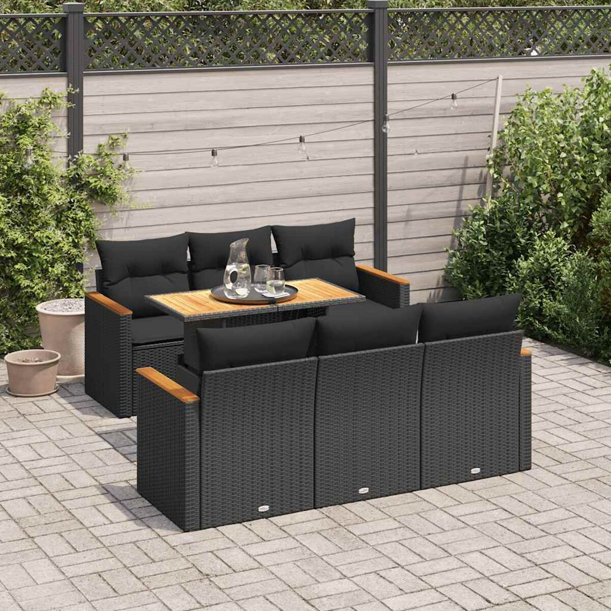 Set patio esterno con mobili in vimini neri, include divano, tavolo e pouf. Su un patio.