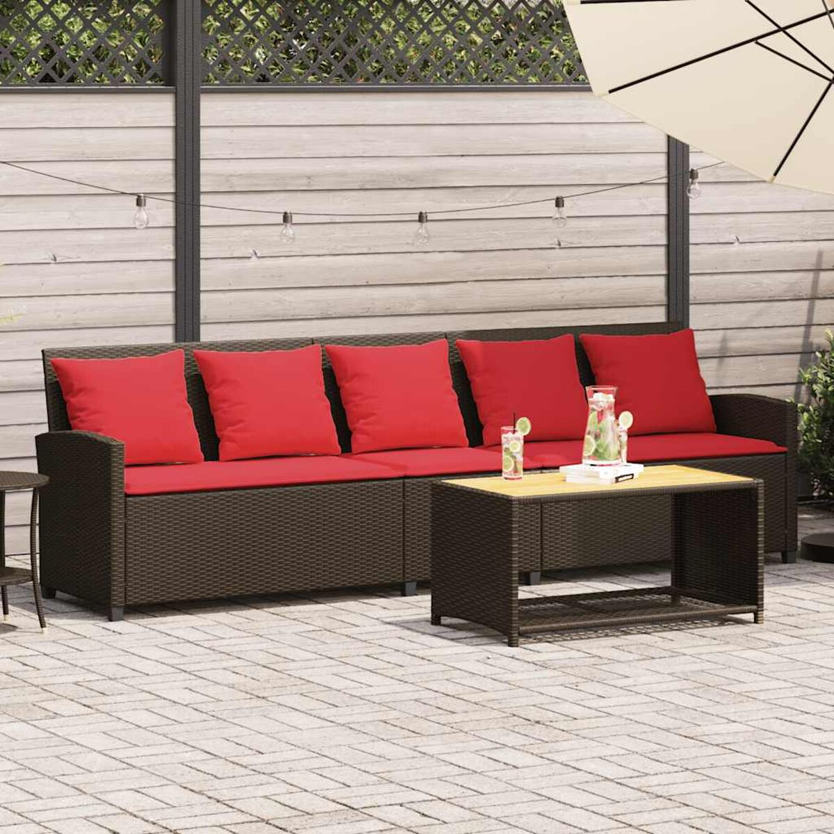 Rattan-Sofa-Set im Freien mit roten Kissen, Tisch, Getränken und Sonnenschirm.
