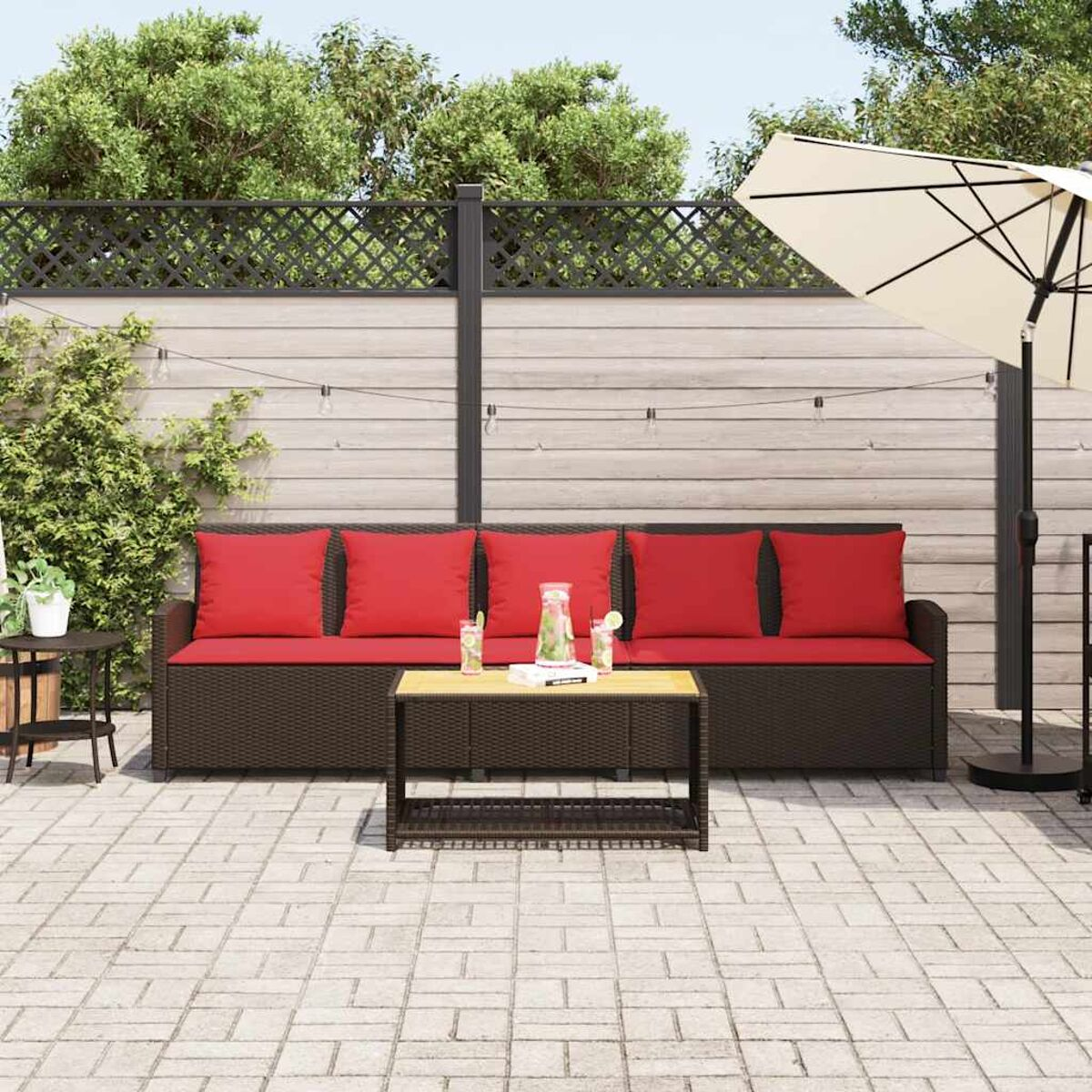 Terrassenecke mit braunem Korbmöbel, roten Kissen und kleinem Tisch. Ein Sonnenschirm ist geöffnet.